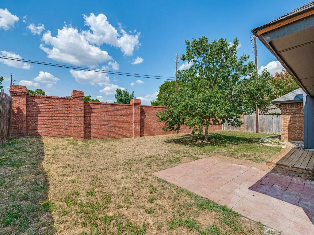 Expansive backyard featuring a brick privacy wall, mature tree, and a paved patio area