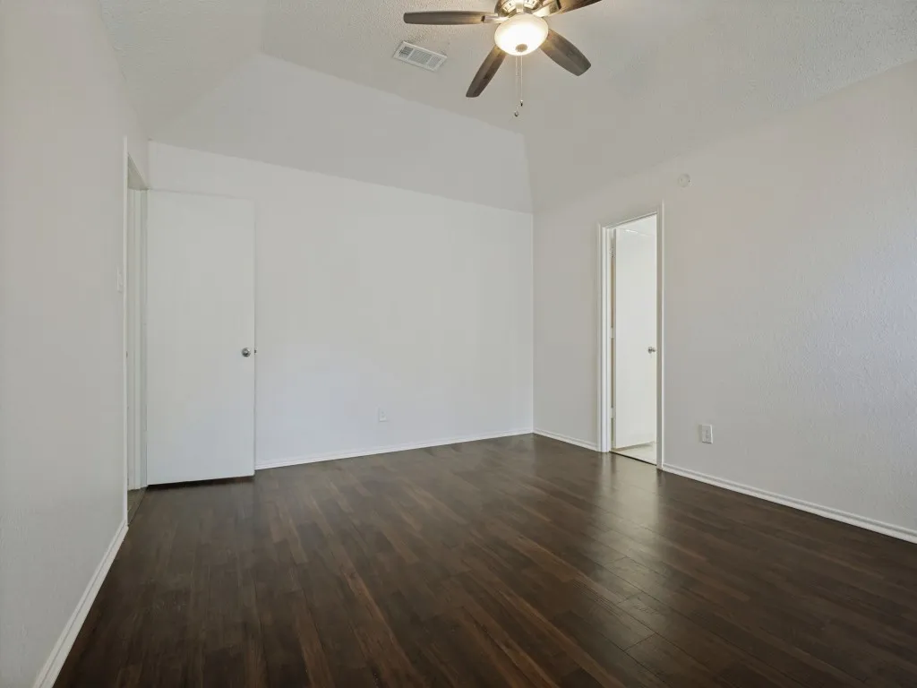 Vaulted ceiling with a ceiling fan, dark wood-finish flooring, and white walls