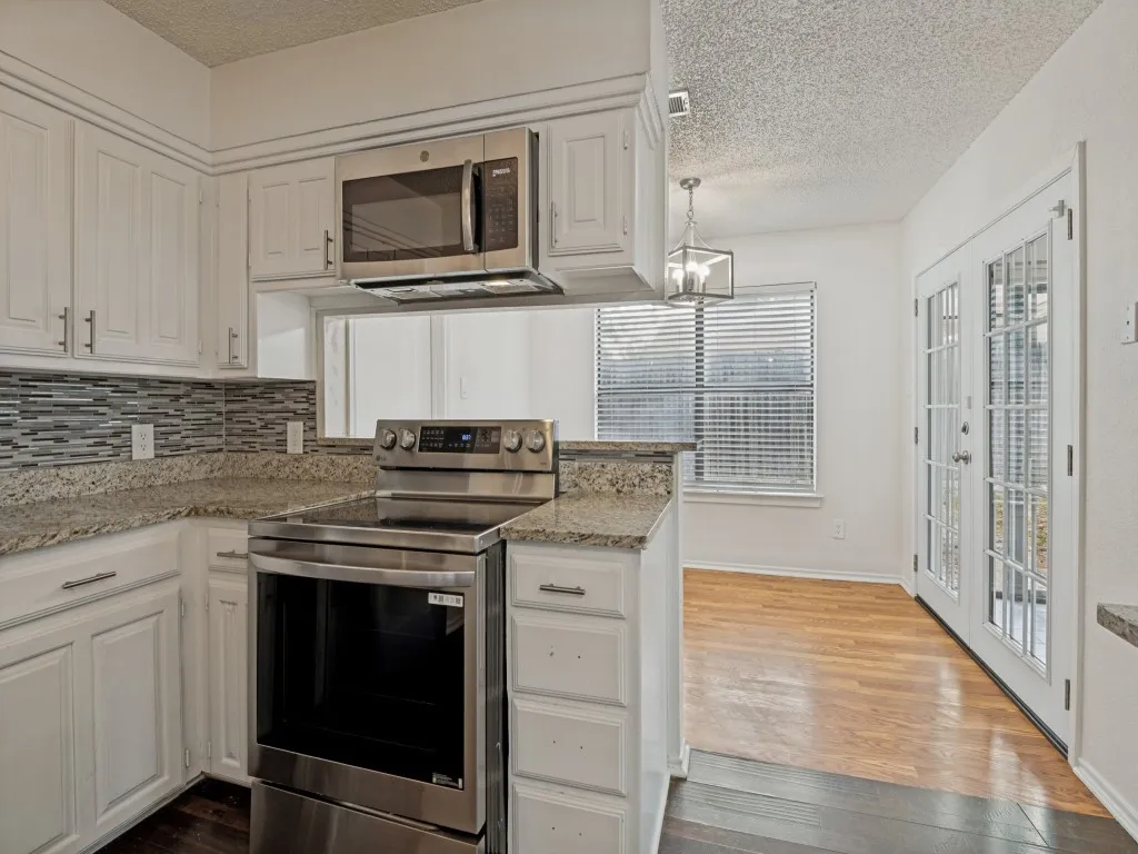 White cabinetry with modern hardware, stainless steel appliances, mosaic tile backsplash, granite countertops, and French doors