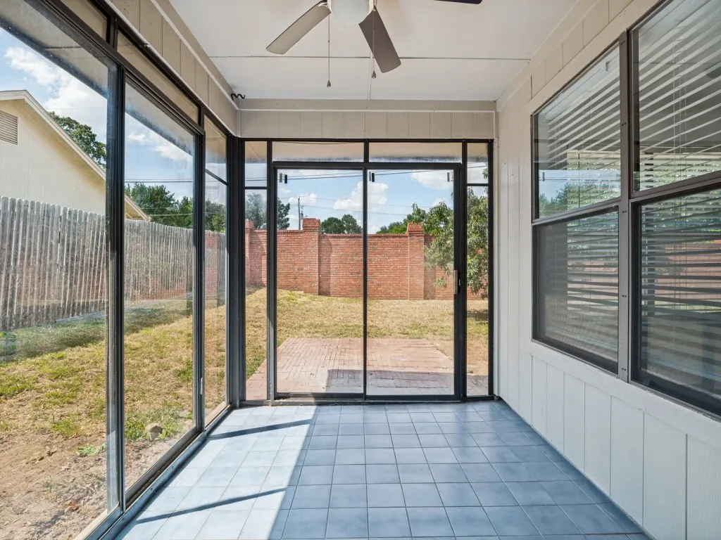 Screened-in porch featuring ceramic tile flooring, a ceiling fan, and large windows