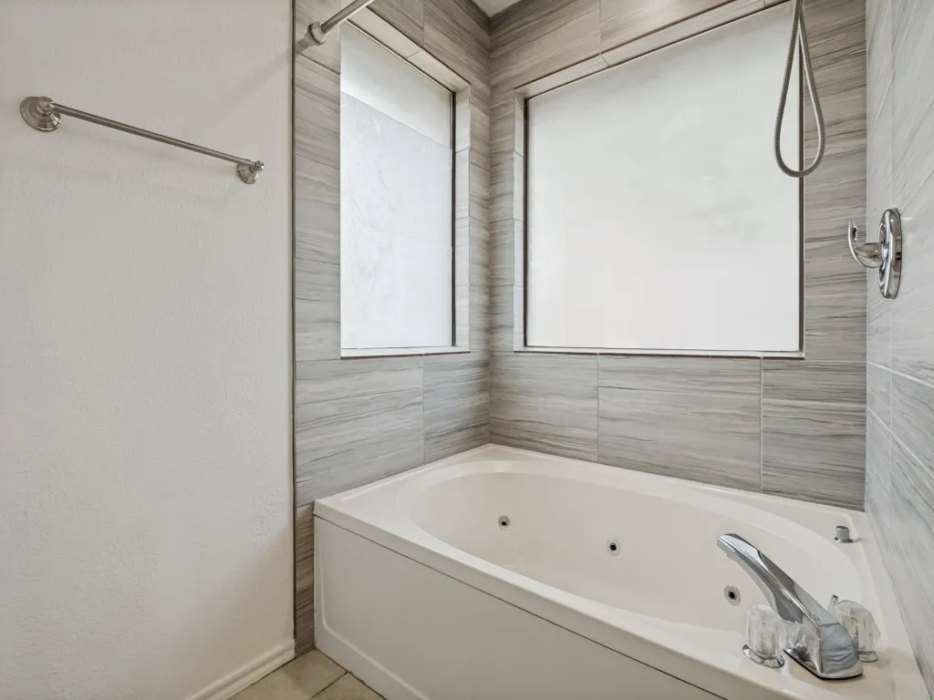 Jetted soaking tub with a deck-mounted faucet, surrounded by large format tile
