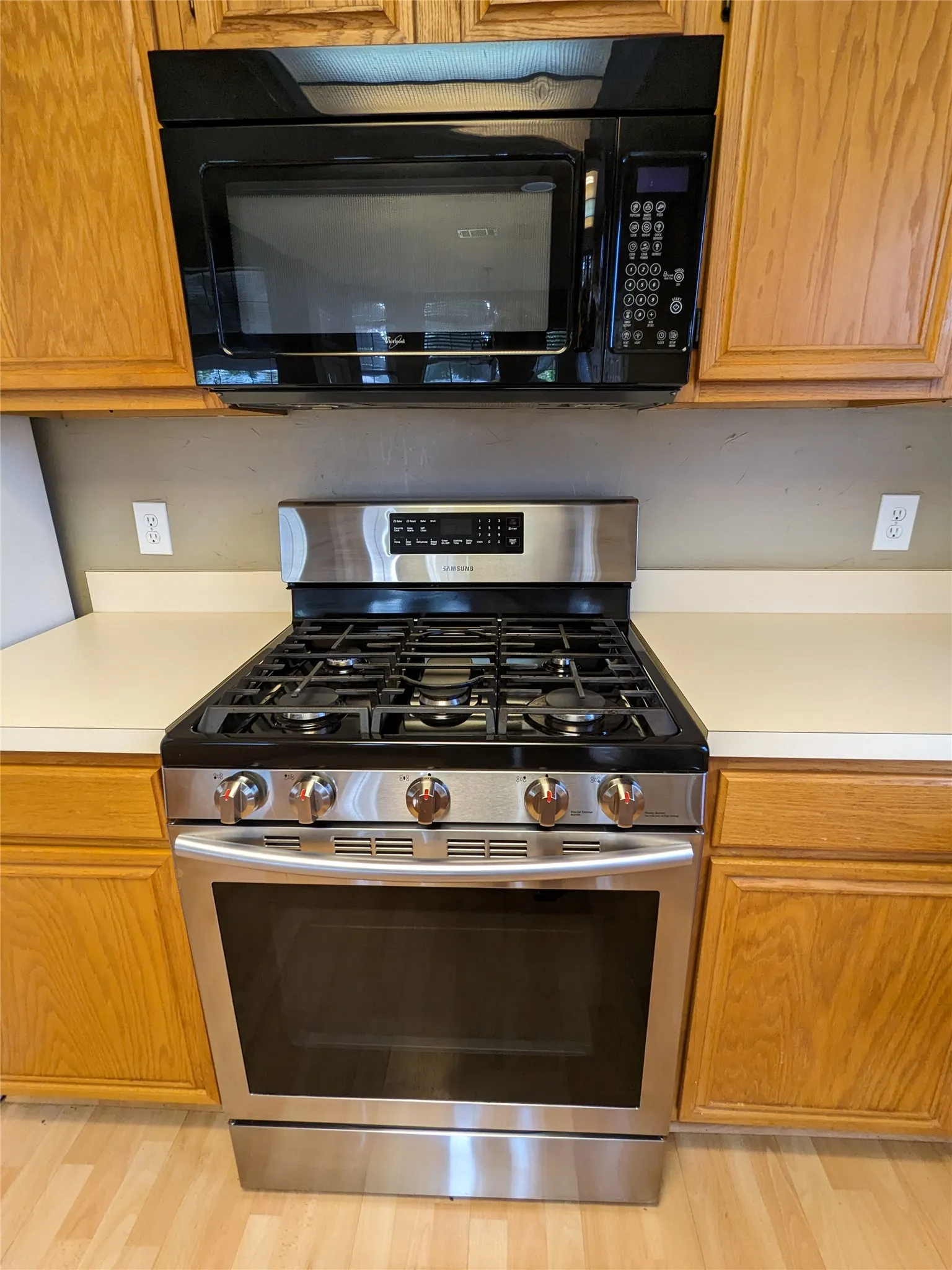 Stainless steel gas range with a coordinating microwave, wood-finish cabinetry, and solid surface countertops