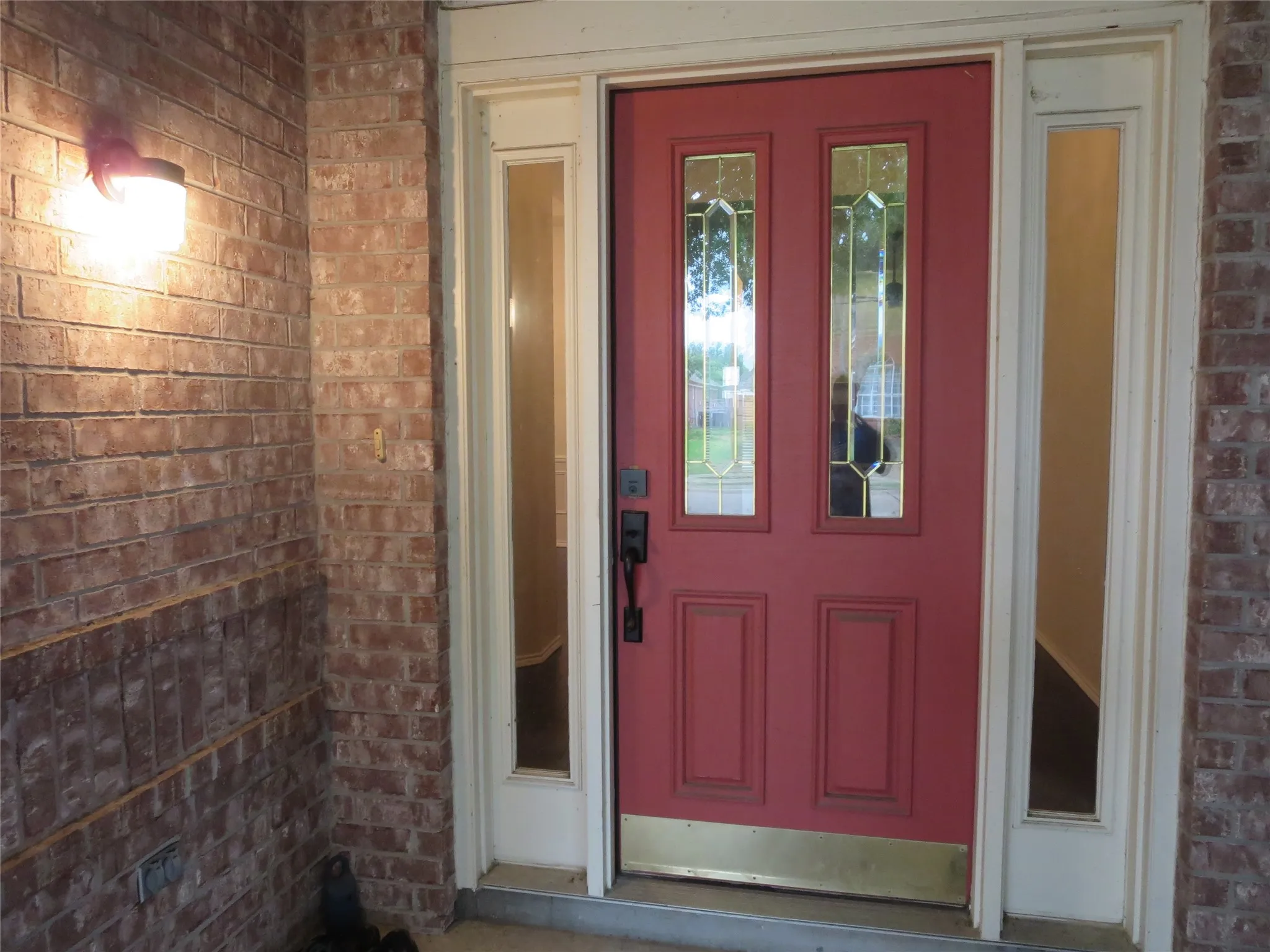 Brick exterior with a red entry door featuring decorative glass inserts and a sidelight