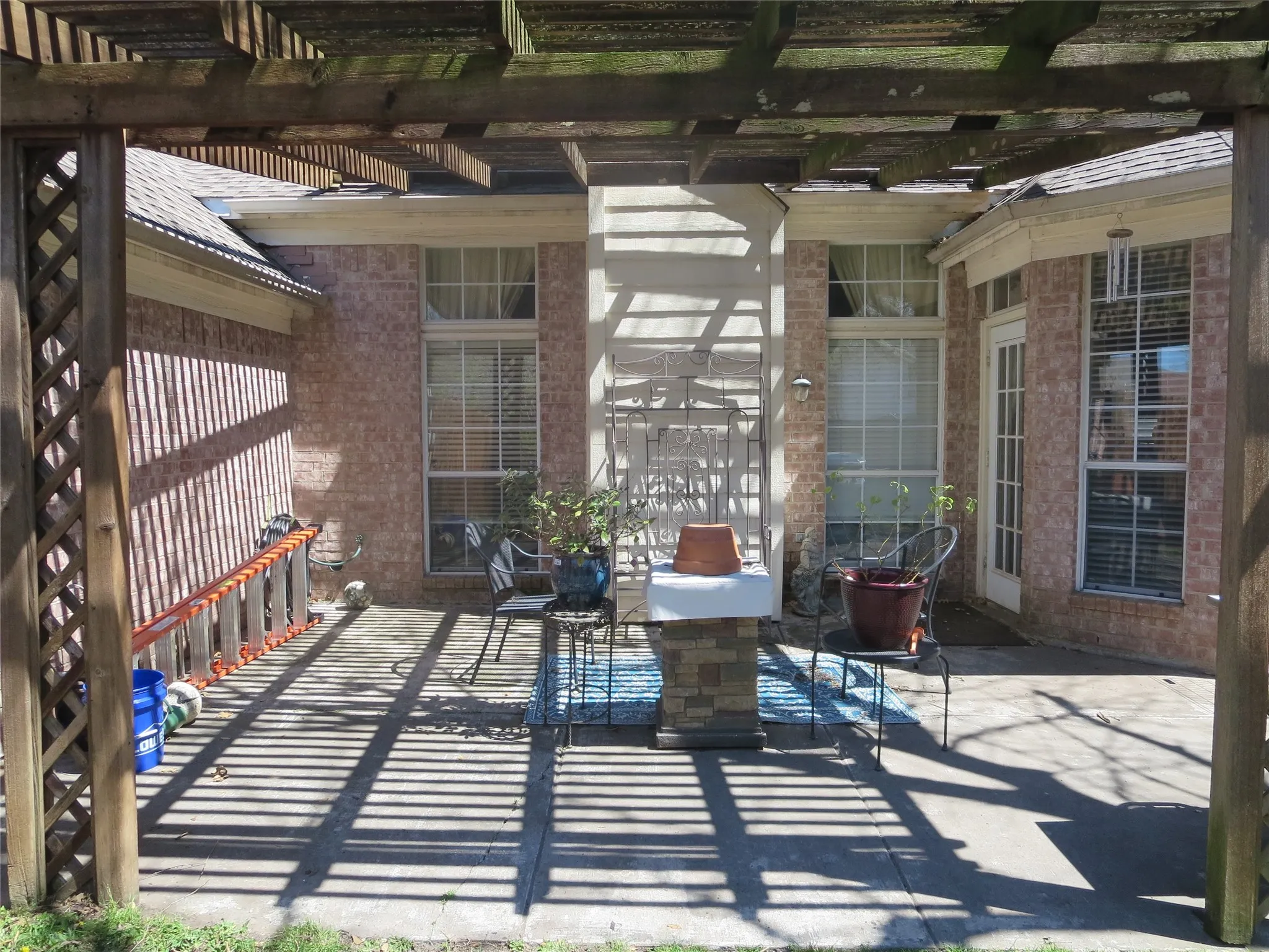 Pergola with lattice side panels, brick exterior, multiple windows, French door, and concrete patio