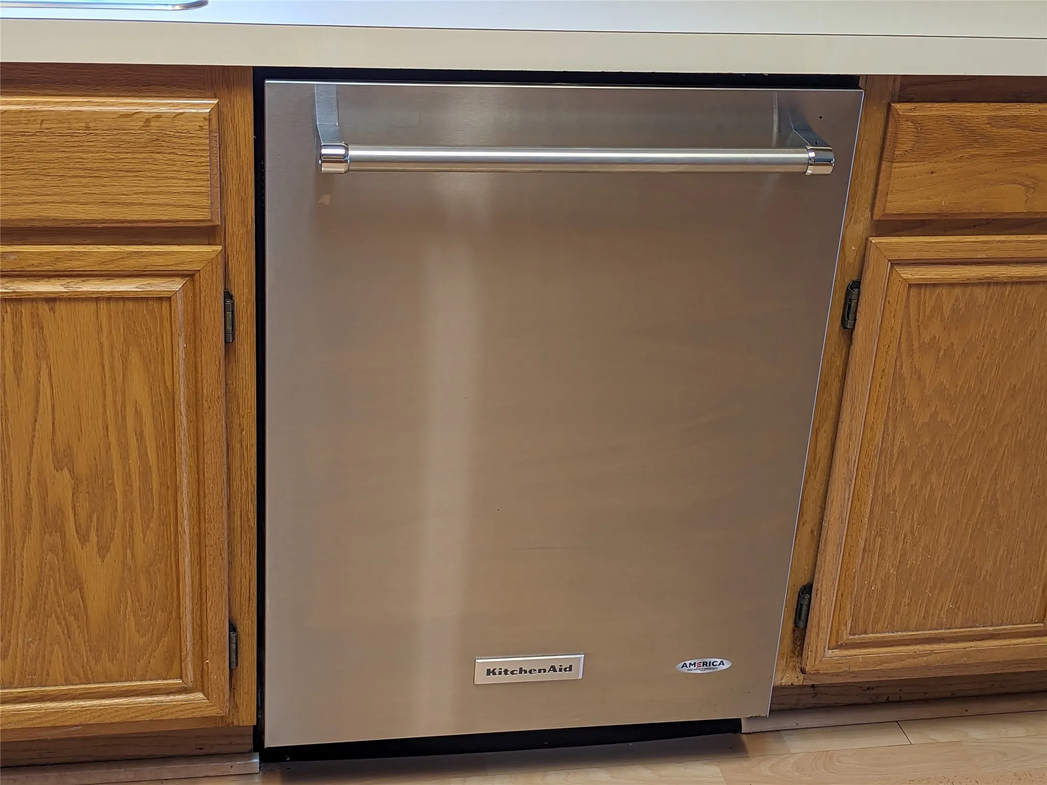 Stainless steel dishwasher with a bar handle, integrated into wood-finish cabinetry