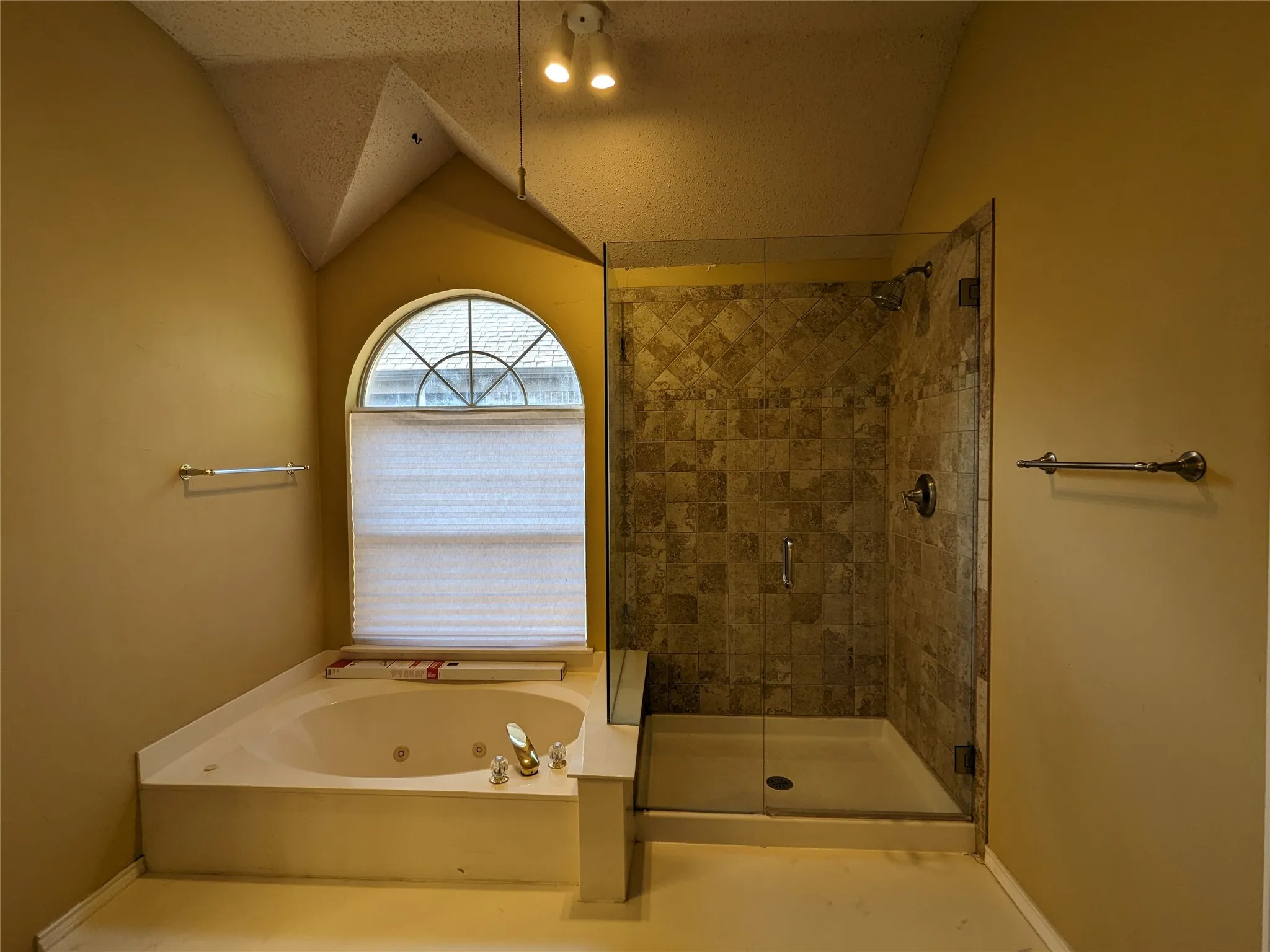 Corner jetted tub with an arched window, tiled walk-in shower with a glass enclosure, and sloped ceiling
