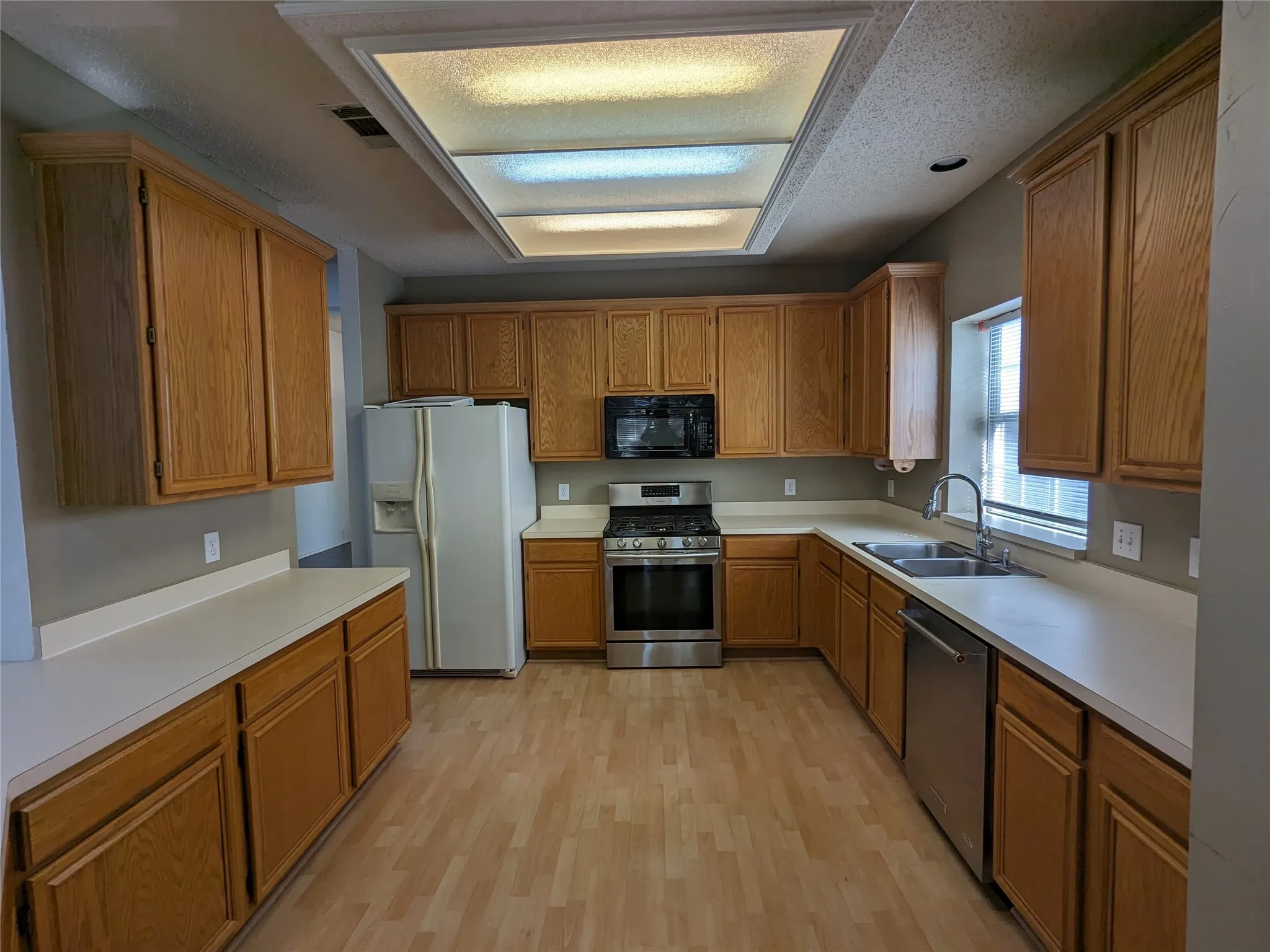 Kitchen featuring light wood-finish cabinetry, solid surface countertops, a stainless steel range, and wood-finish flooring