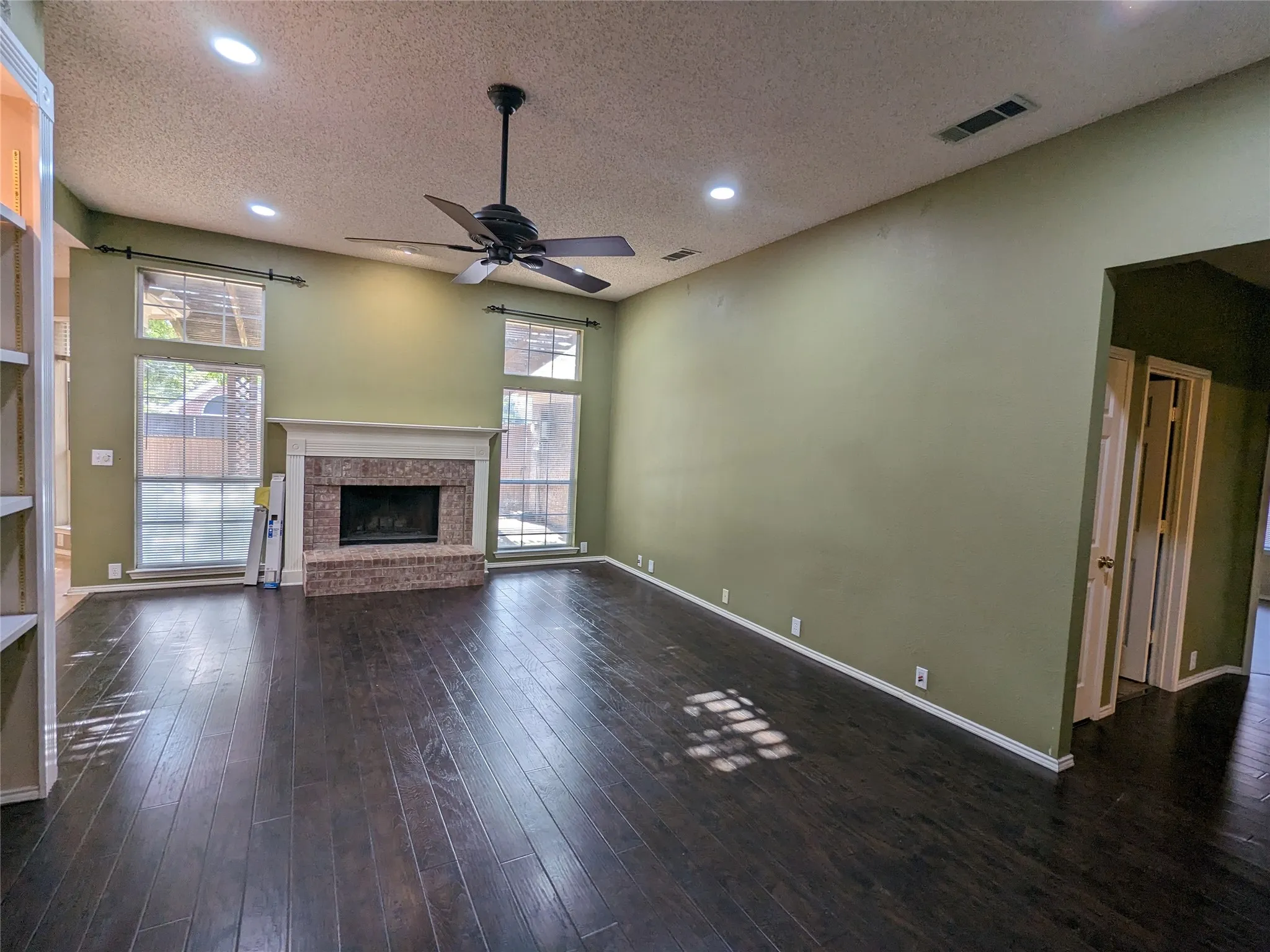 Spacious interior with vaulted ceiling, recessed lighting, dark wood-finish flooring, and a brick fireplace with a stone mantel