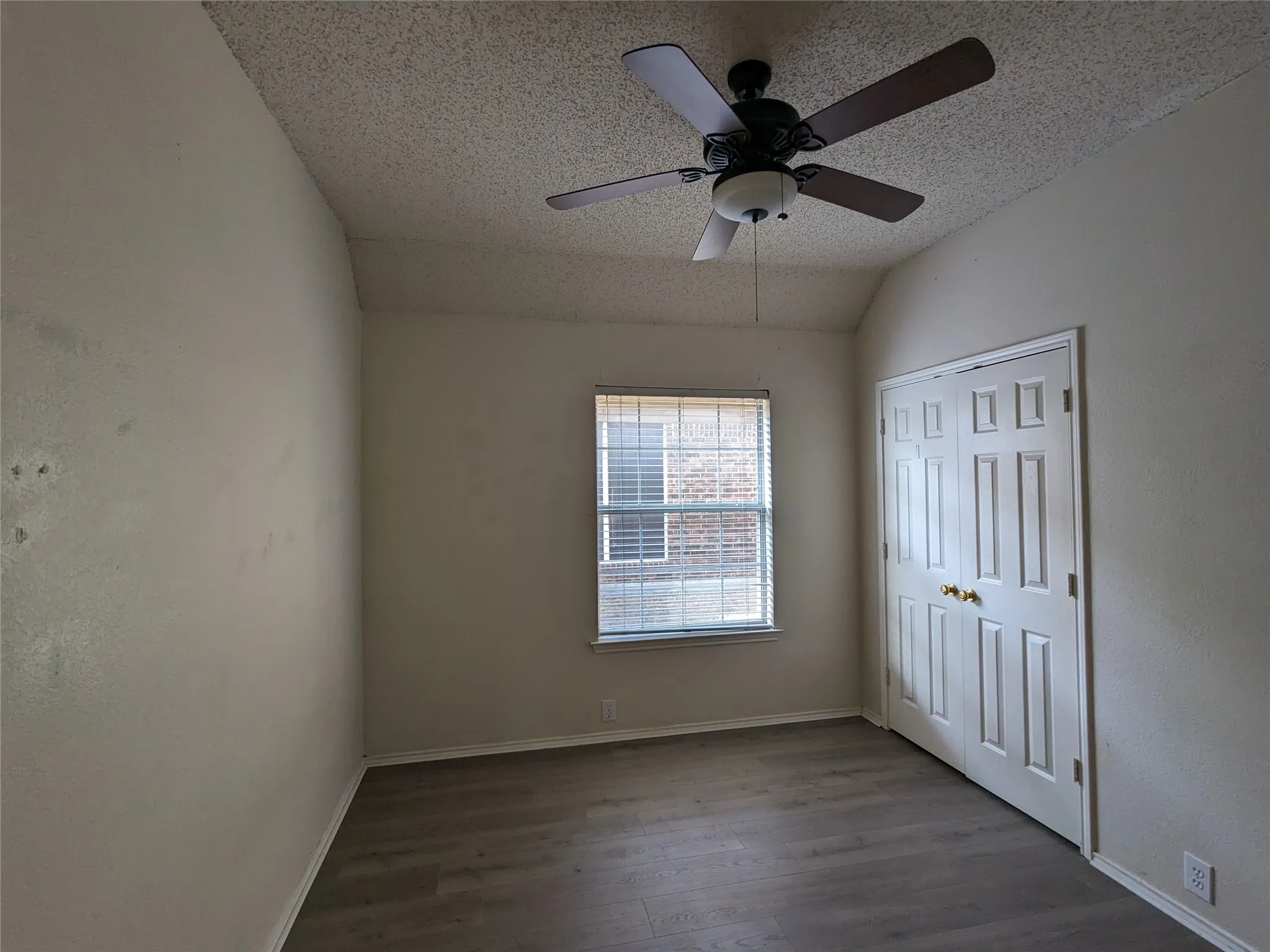 Spacious bedroom with ceiling fan and integrated lighting, dark wood-finish flooring, and abundant natural light from large window