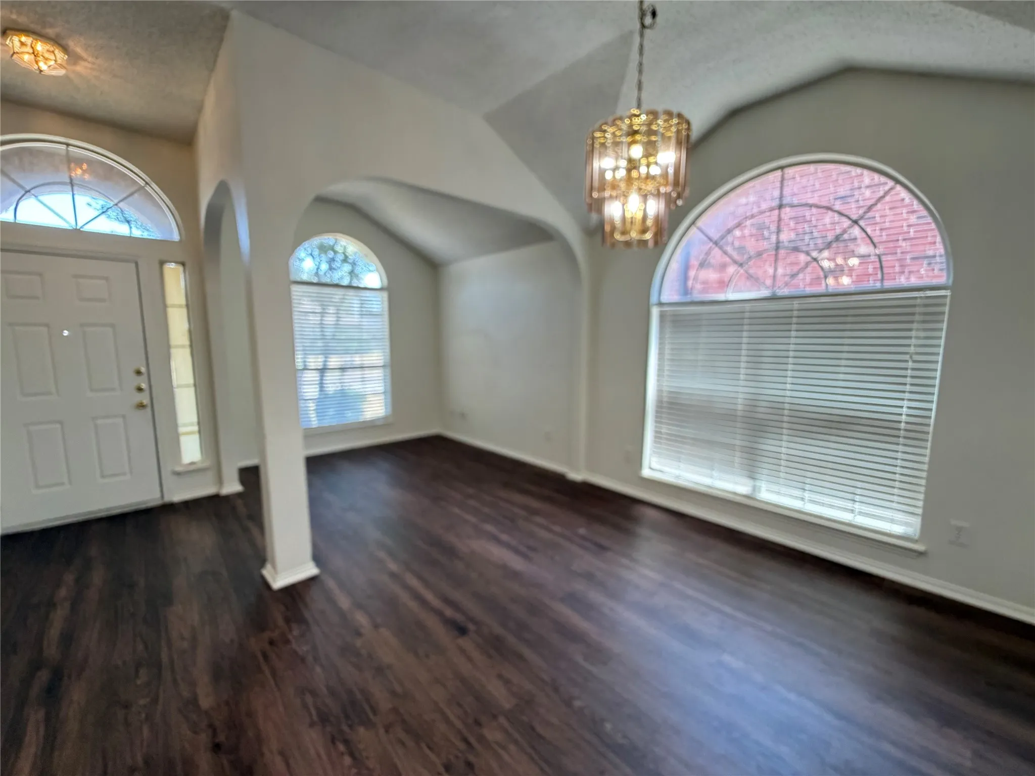 Wood-finish flooring, vaulted ceiling, arched doorway, decorative chandelier, and arched transom windows
