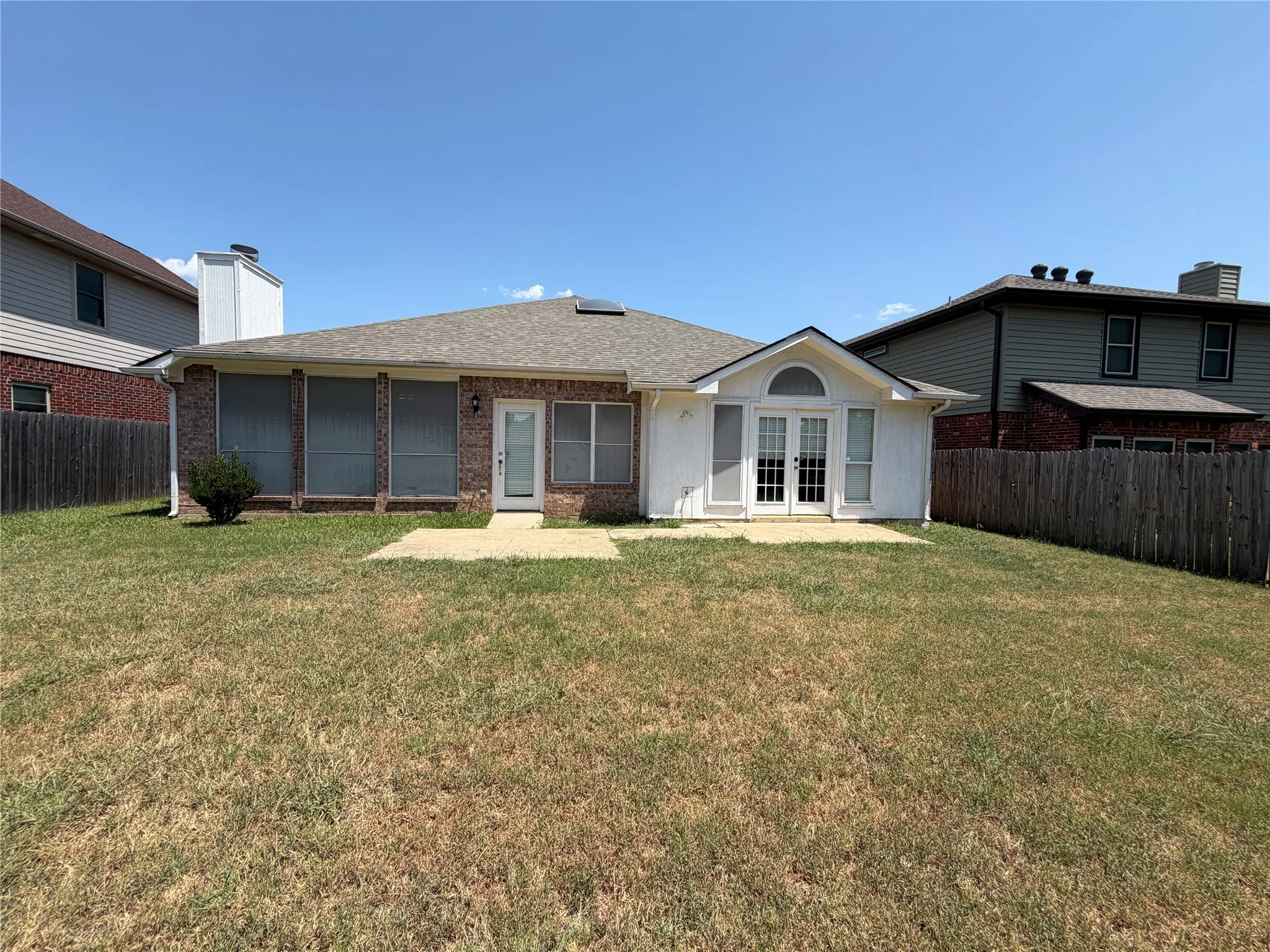 Expansive backyard featuring a brick exterior, white painted siding, a screened patio, and a separate patio area with French doors