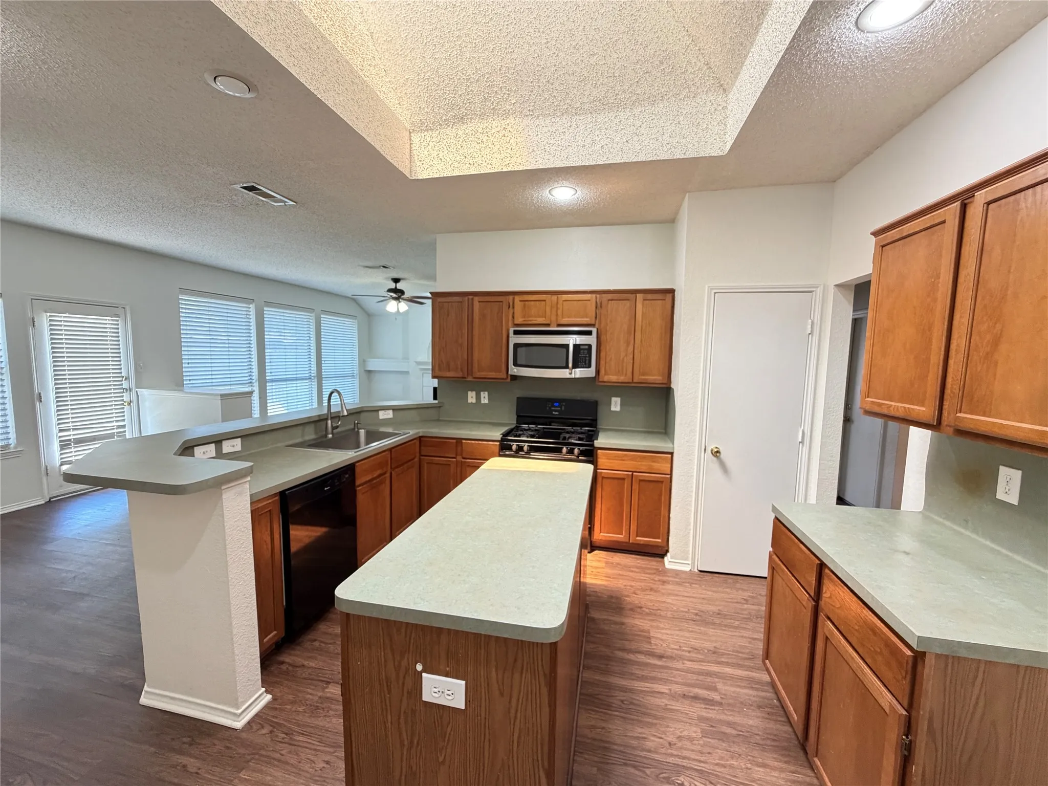 Kitchen featuring wood-finish flooring, wood cabinetry, stainless steel appliances, a center island, and a breakfast bar
