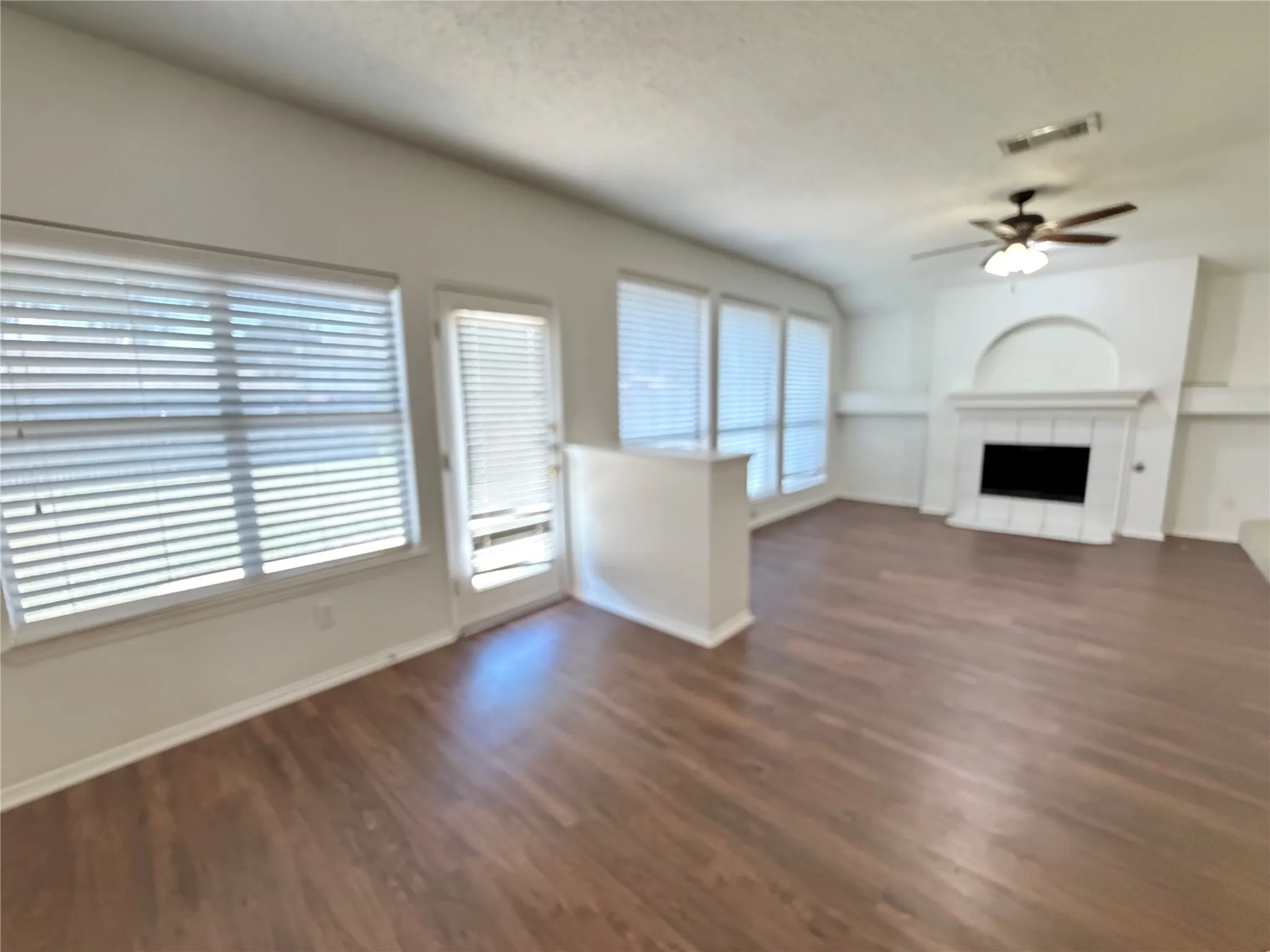 Wood-finish flooring, multiple windows with blinds, built-in fireplace, ceiling fan with light fixture, and a white interior door