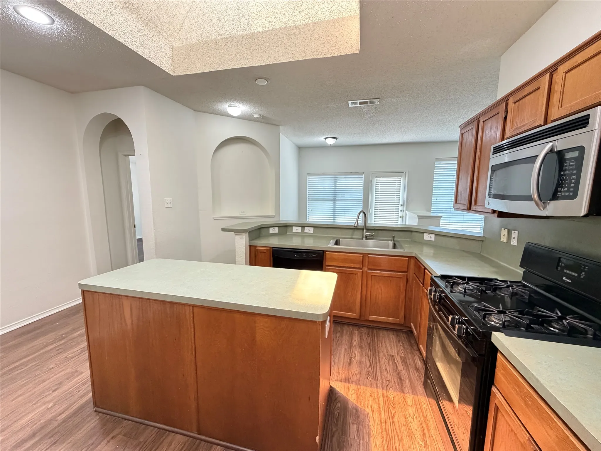 Kitchen featuring wood-finish flooring, an island with countertop, wood cabinetry, a gas range, and a built-in microwave