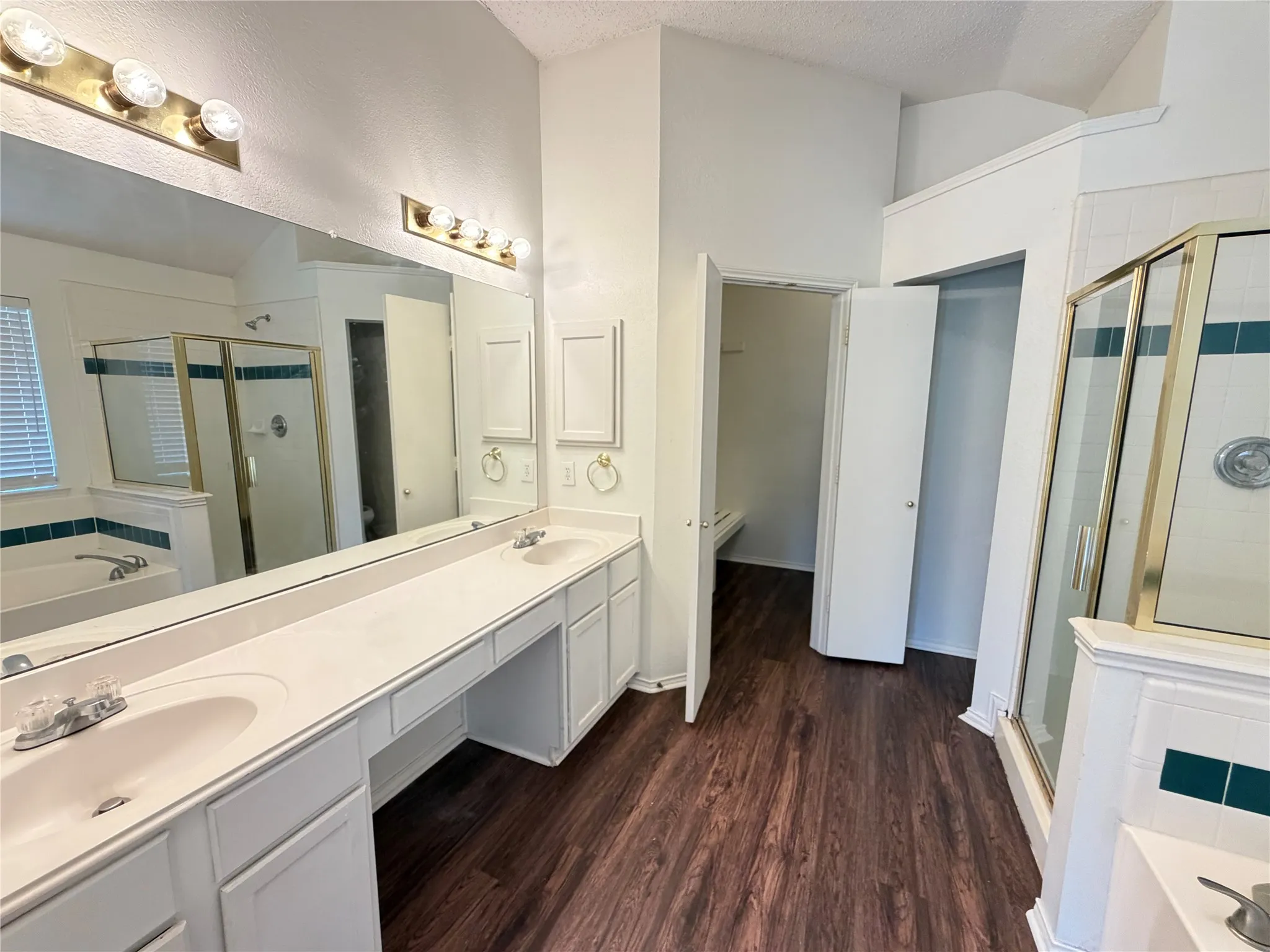 Dual sink vanity with ample countertop space, wood-finish flooring, and a glass-enclosed shower