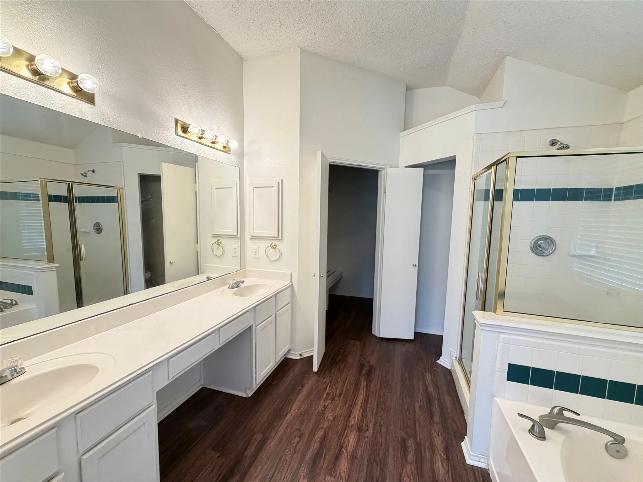 Dual vanity with integrated sinks, wood-finish flooring, built-in cabinetry, and a shower enclosure