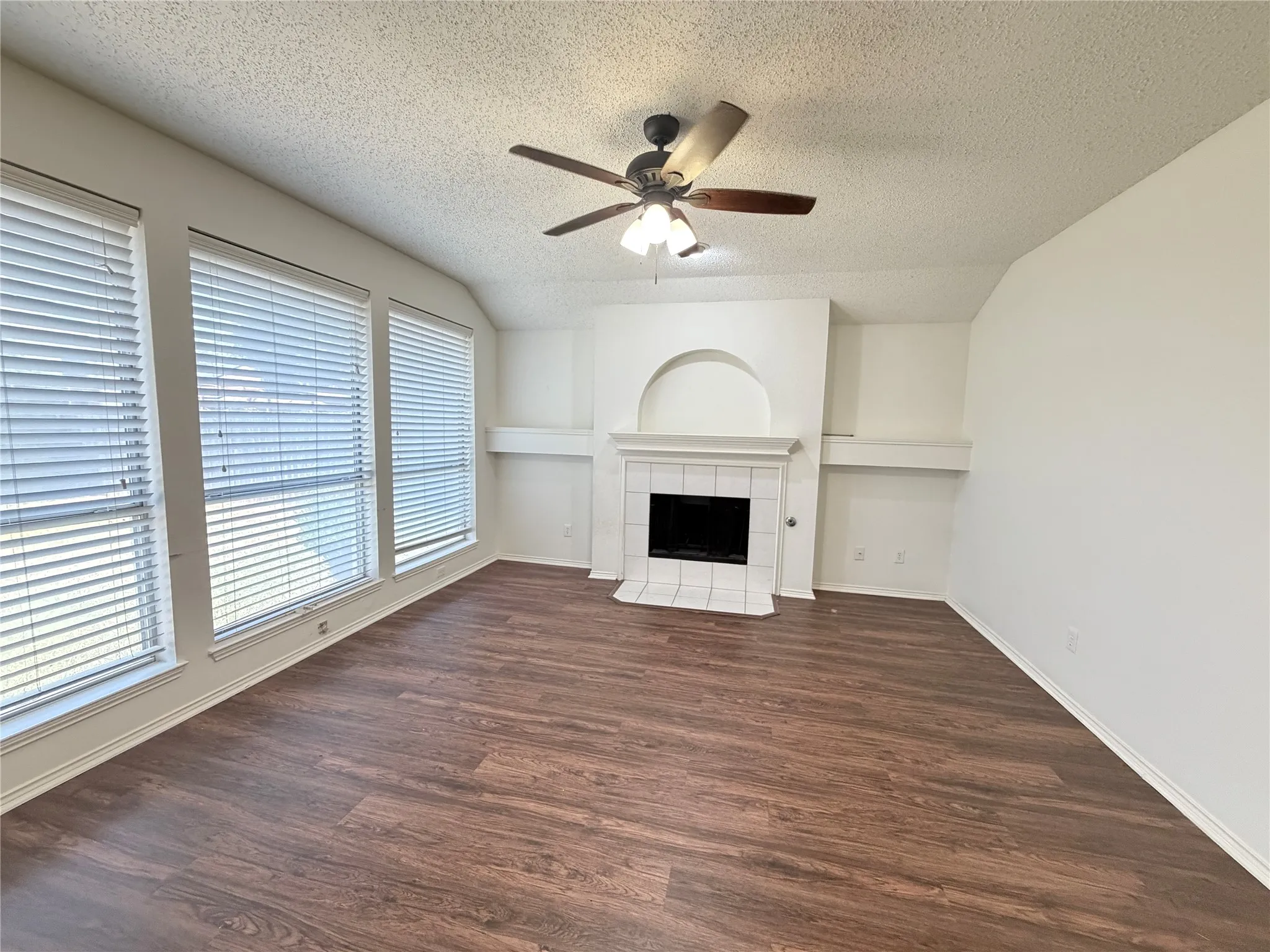 Wood-finish flooring, multiple large windows, and a tiled fireplace with an arched niche