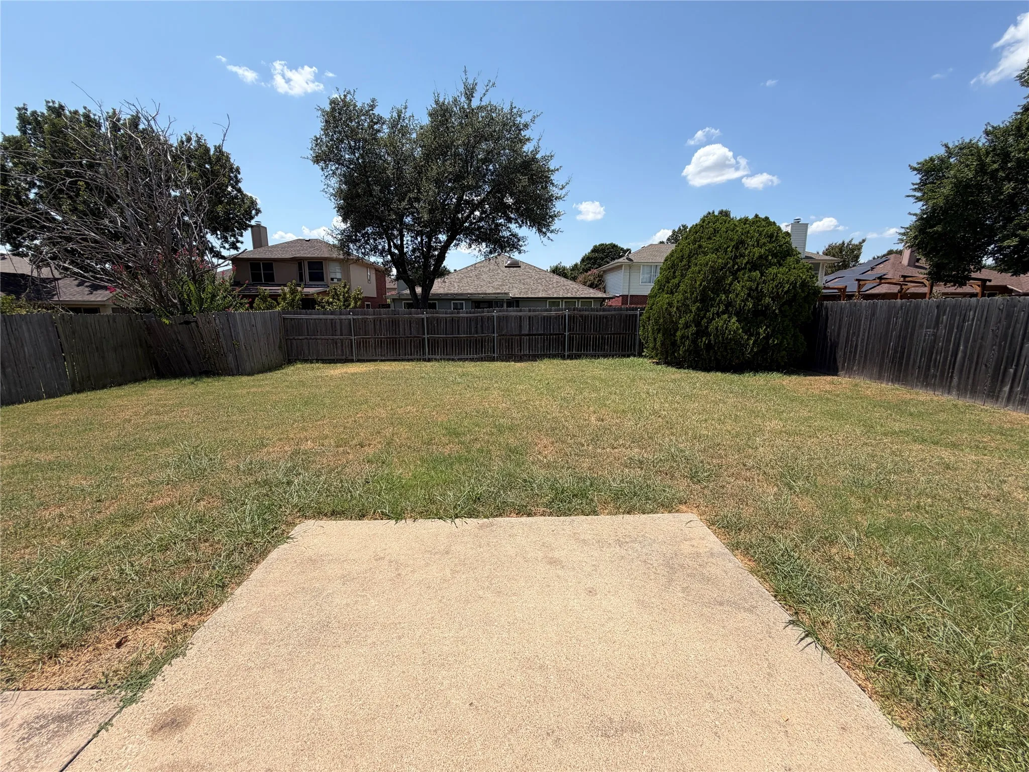 Expansive backyard featuring a concrete patio, wood fencing, and mature trees
