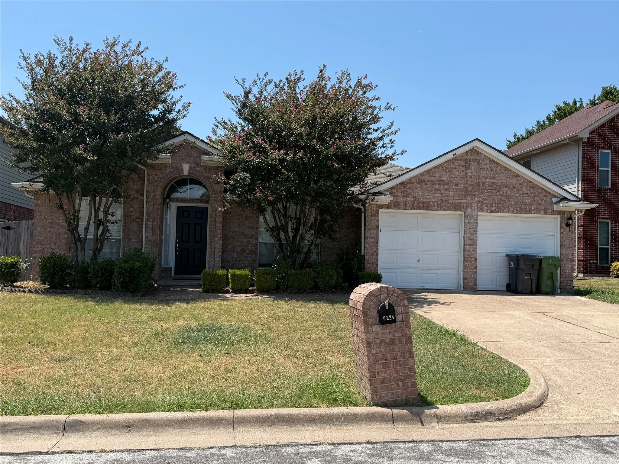 Brick exterior featuring a two-car garage, concrete driveway, and arched entry