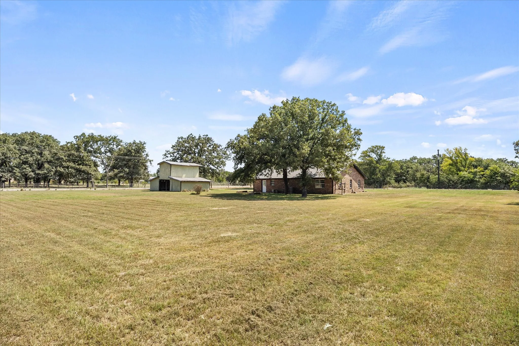 Expansive grass acreage with mature trees, a brick residence, and a multi-level auxiliary building
