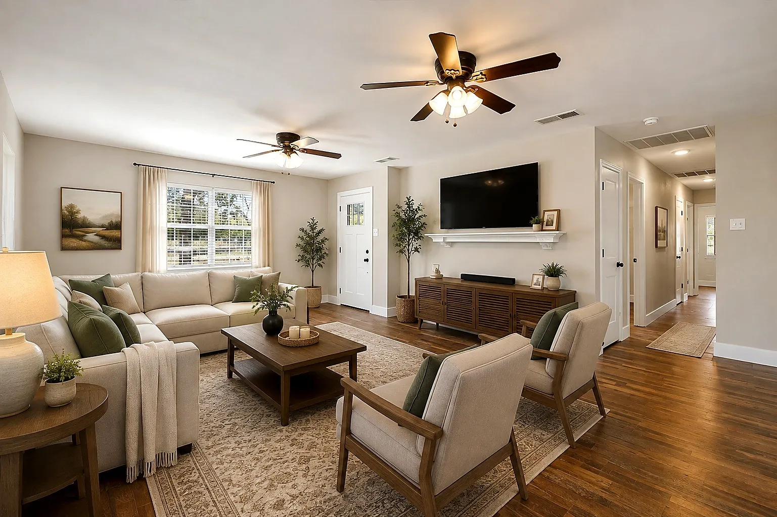 Light-filled living area with wood-finish flooring, two ceiling fans, and a white paneled door