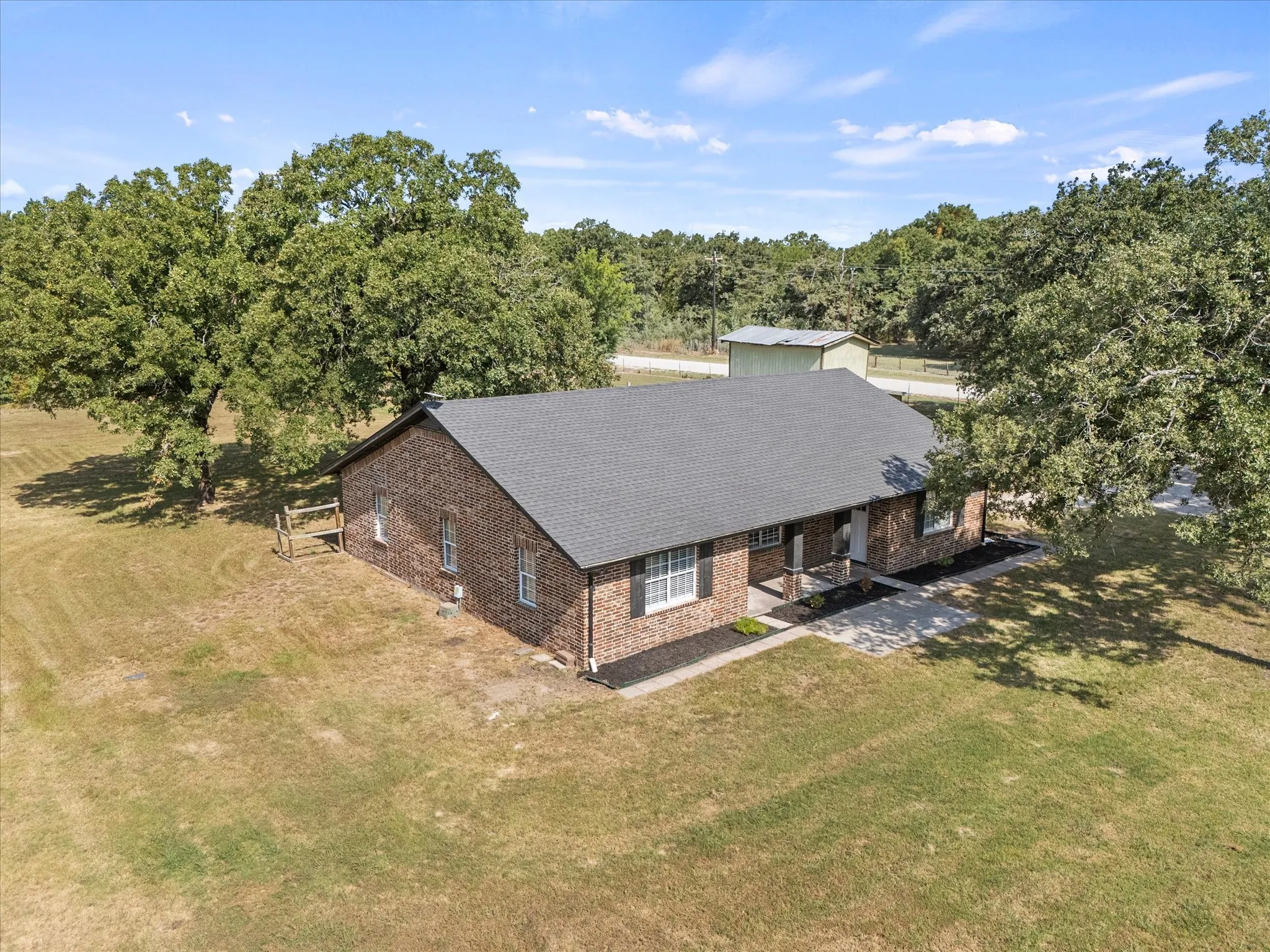 Brick exterior residence with a dark shingle roof, established landscaping, and a concrete walkway