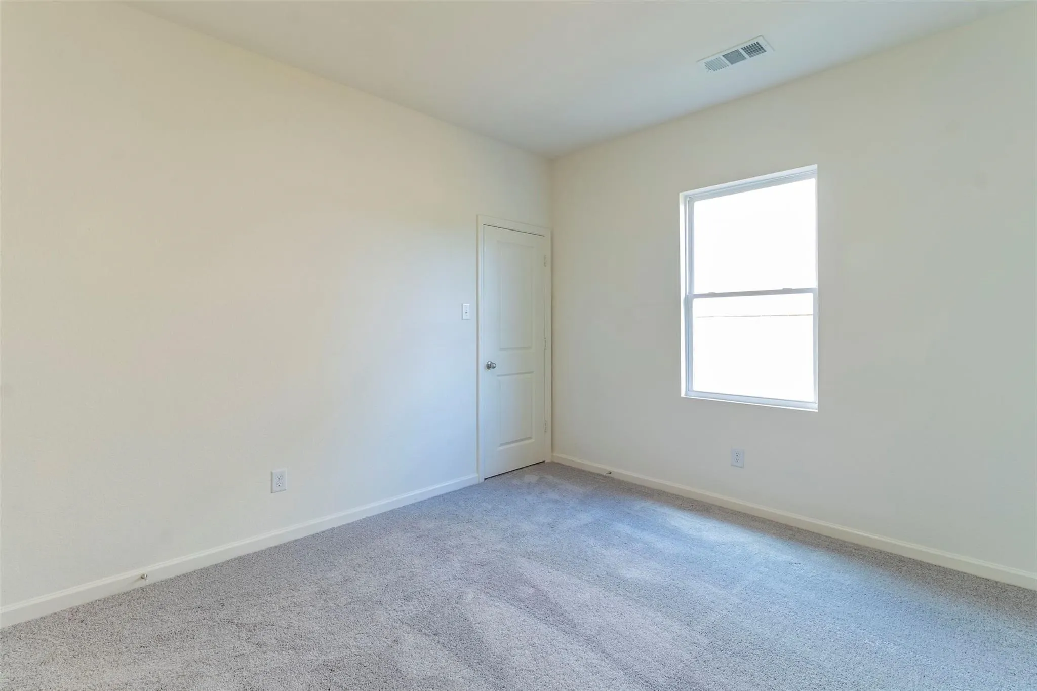 Wall-to-wall carpeting in a neutral tone, light-colored painted walls, and a single window with white trim