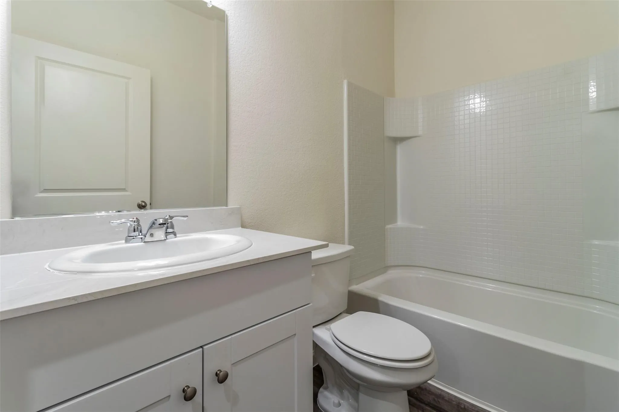 Vanity with integrated sink, chrome faucet, wall-mounted mirror, and a full bathtub with tile-patterned surround