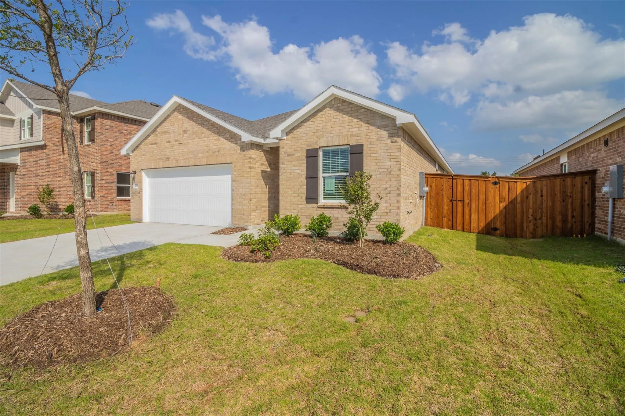 Brick exterior with white trim, attached garage with a white door, concrete driveway, and wood privacy fence