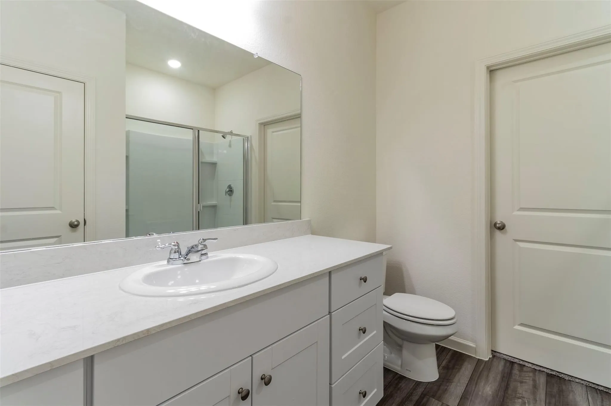 White vanity with an integrated sink and chrome faucet, large rectangular mirror, and wood-finish flooring