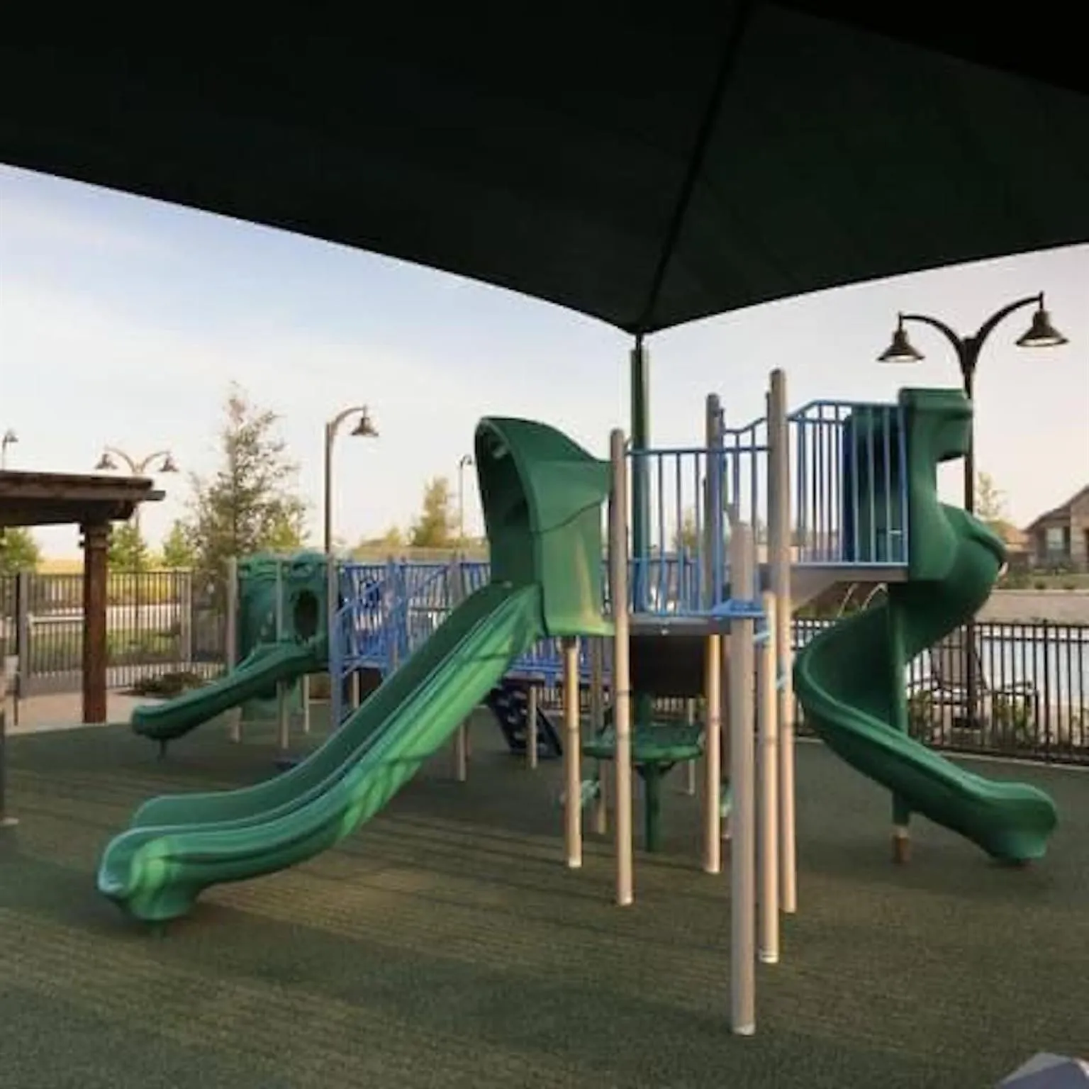 Playground area featuring multiple slides, climbing structures, a shade canopy, and safety surfacing
