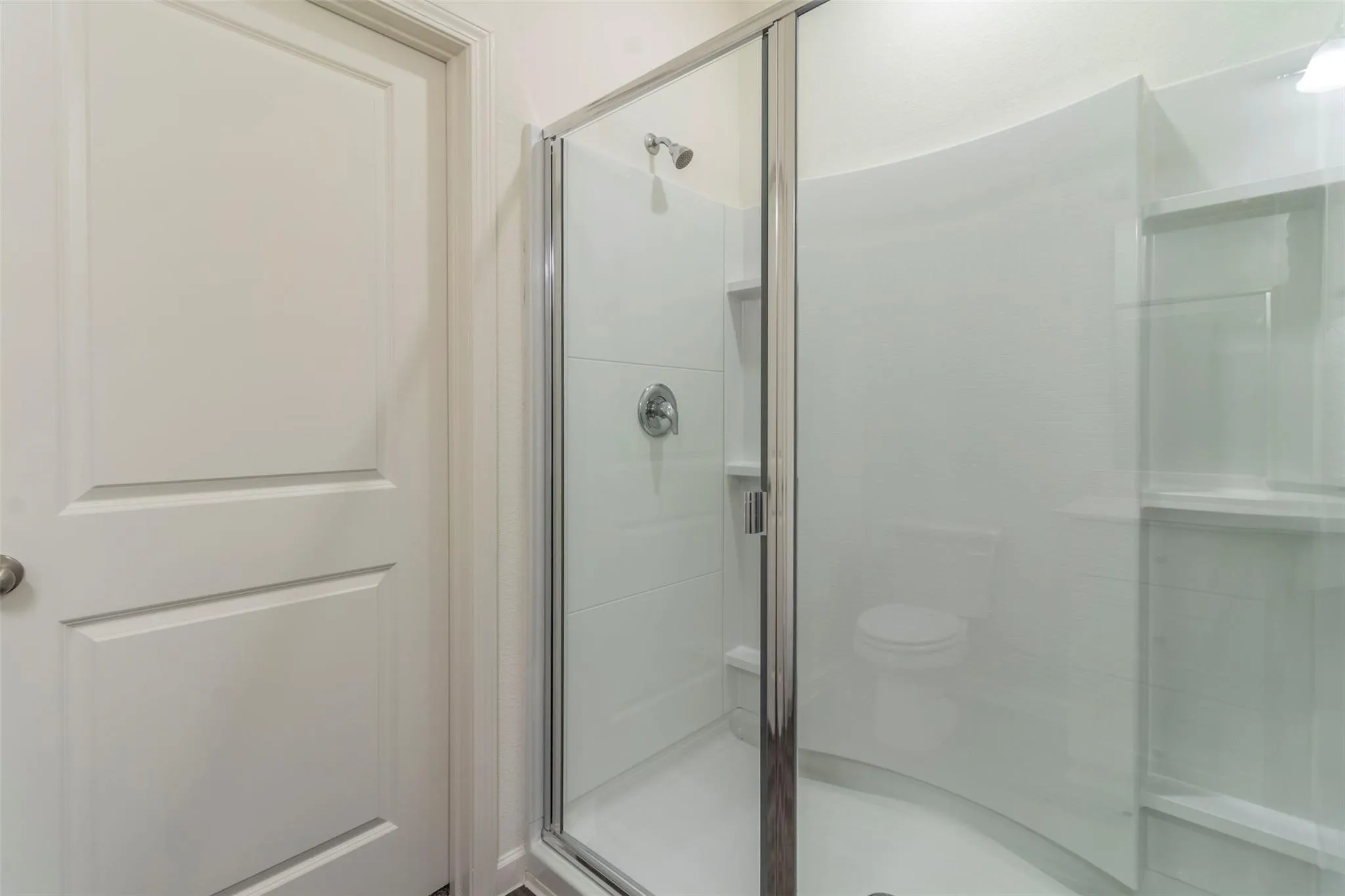 Glass-enclosed shower with a curved frame, integrated shelving, and a chrome showerhead