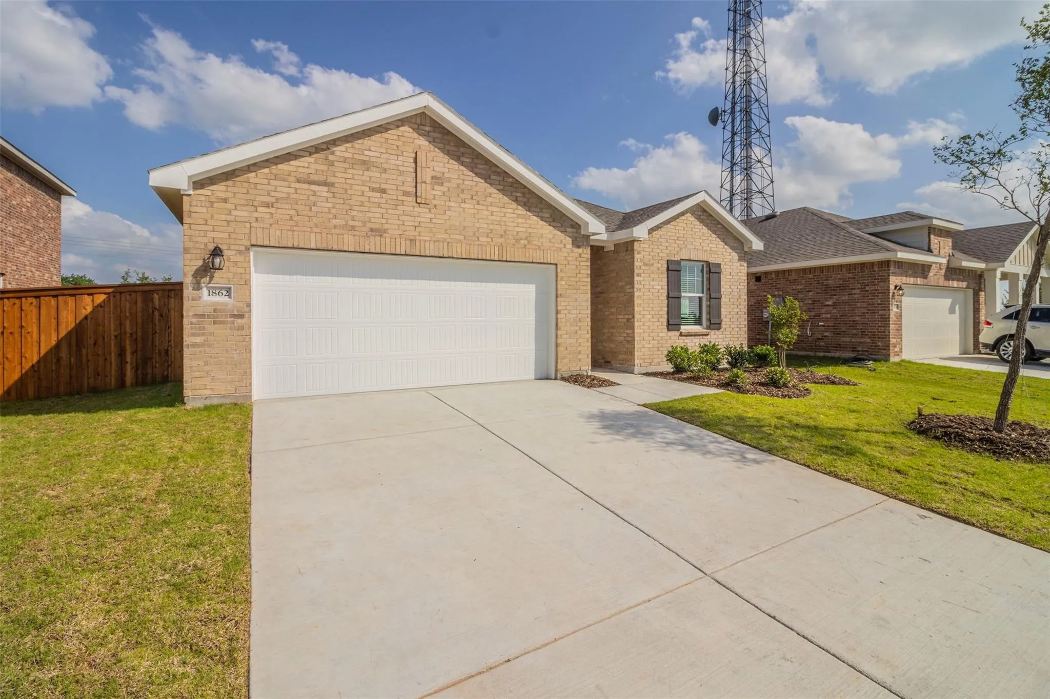 Brick exterior with a two-car garage, concrete driveway, and landscaped front yard