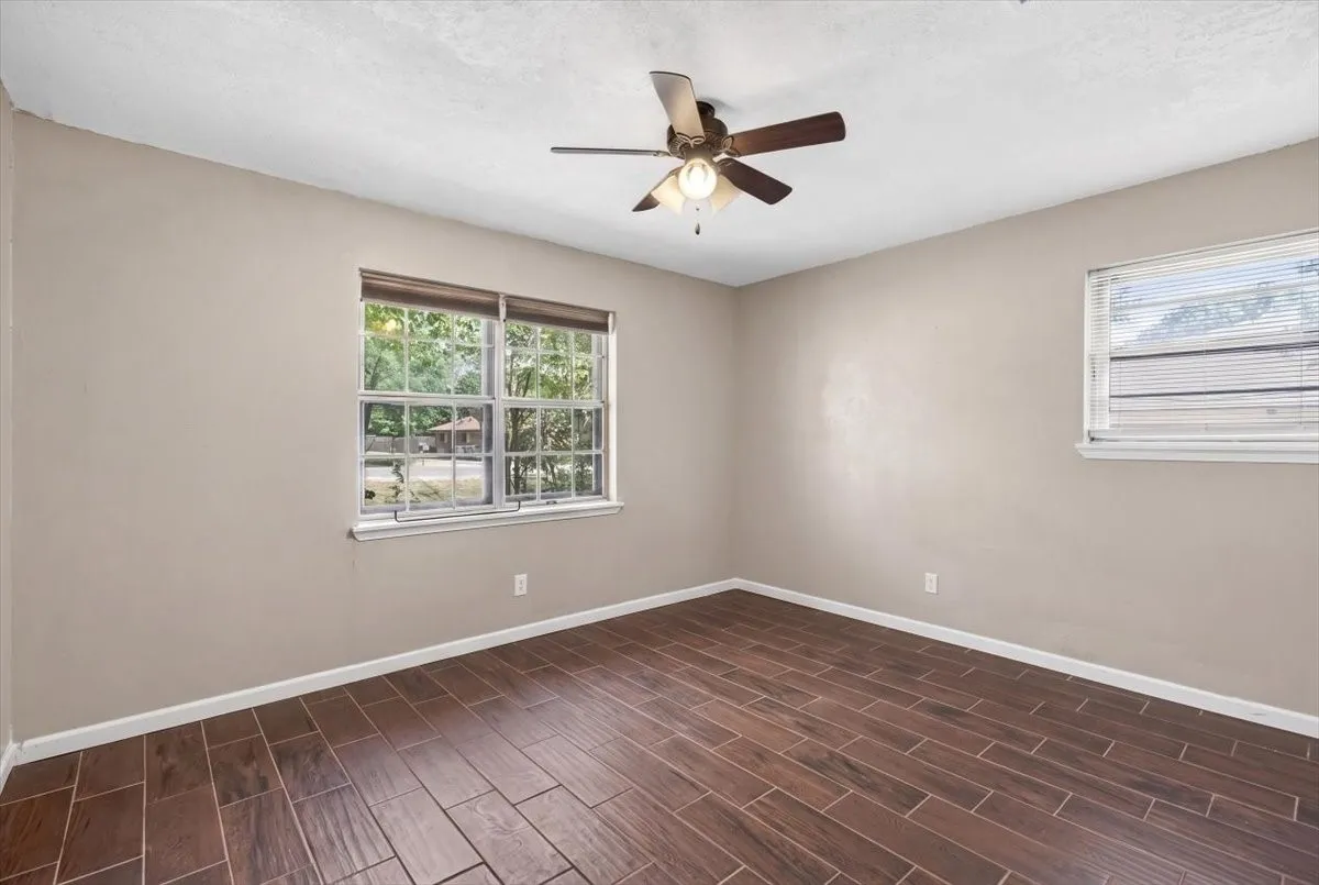 Secondary bedroom with wood looking ceramic tile, ceiling fan and lots of windows for natural light