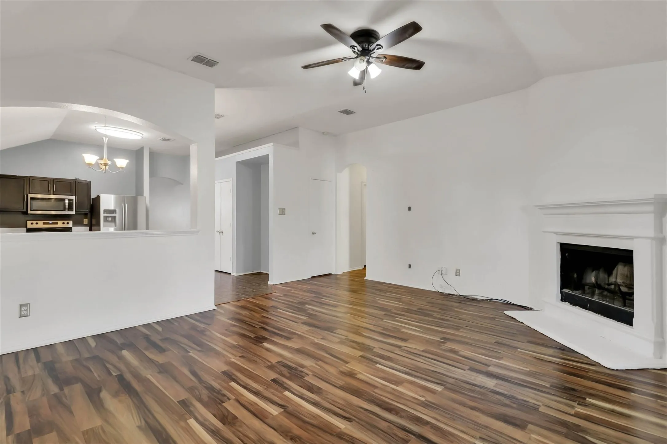 Spacious living area featuring wood-finish flooring, an arched entryway, a built-in fireplace, and a ceiling fan