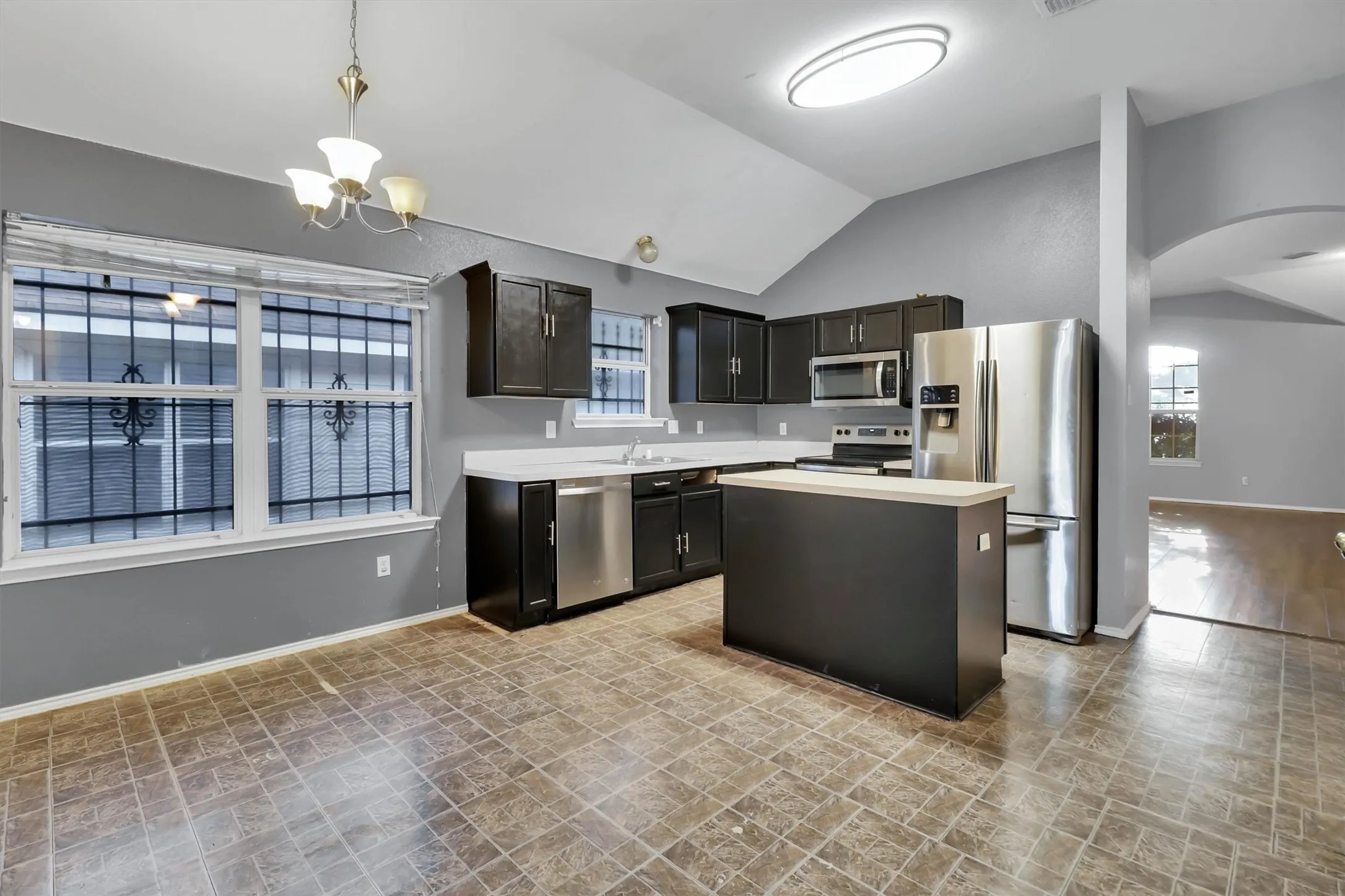 Kitchen featuring dark cabinetry, stainless steel appliances, a center island with a light-toned countertop, and vaulted ceilings