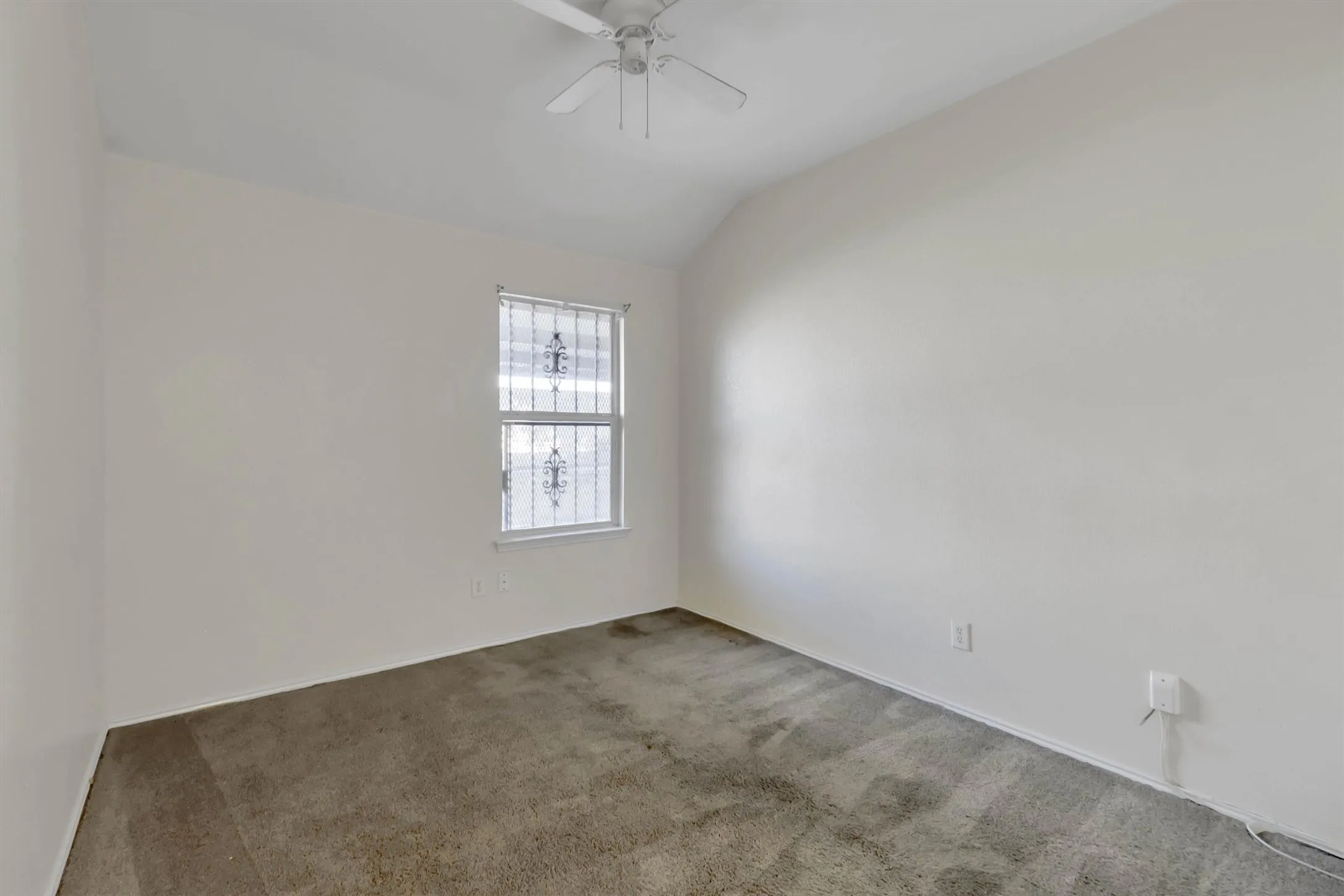Neutral wall tones, window with security bars, ceiling fan, and carpeted flooring