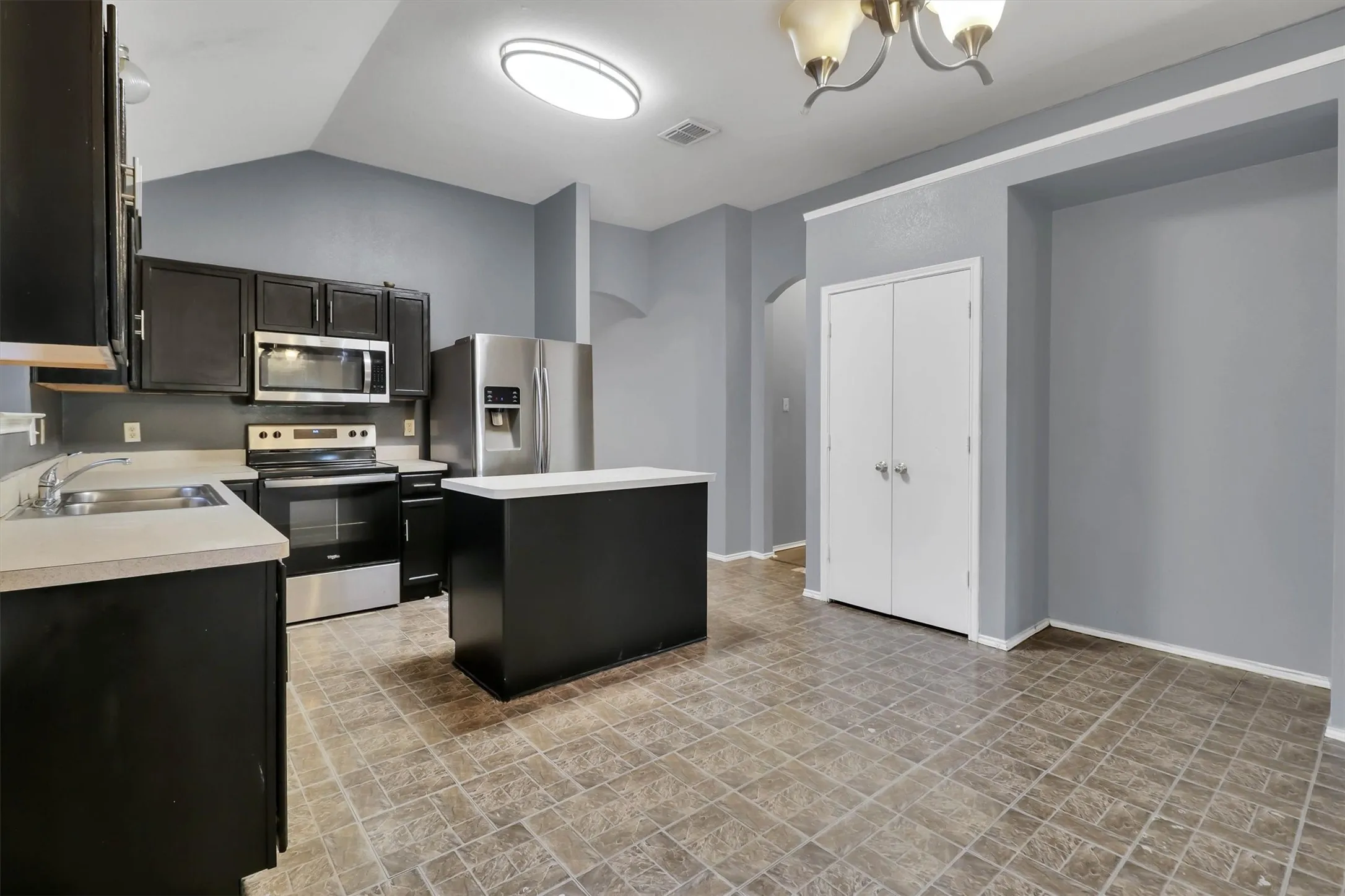 Kitchen featuring black cabinetry, stainless steel appliances, a center island with a light-toned countertop, and patterned floor tiling