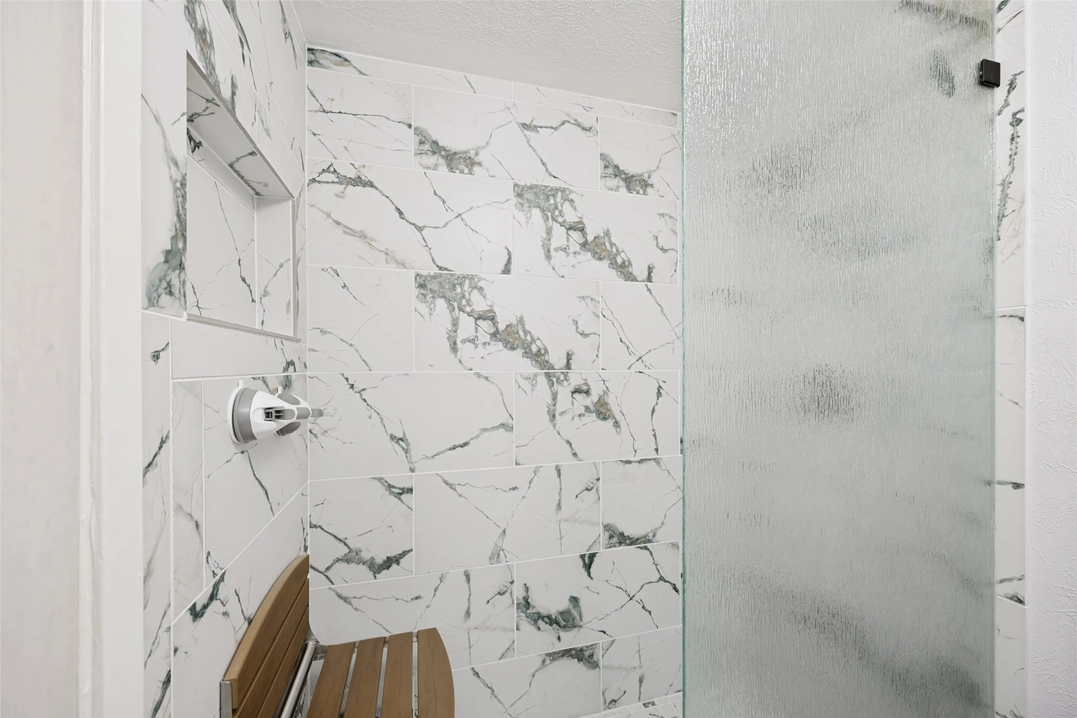 Updated shower with built-in niche and frosted glass door and chair