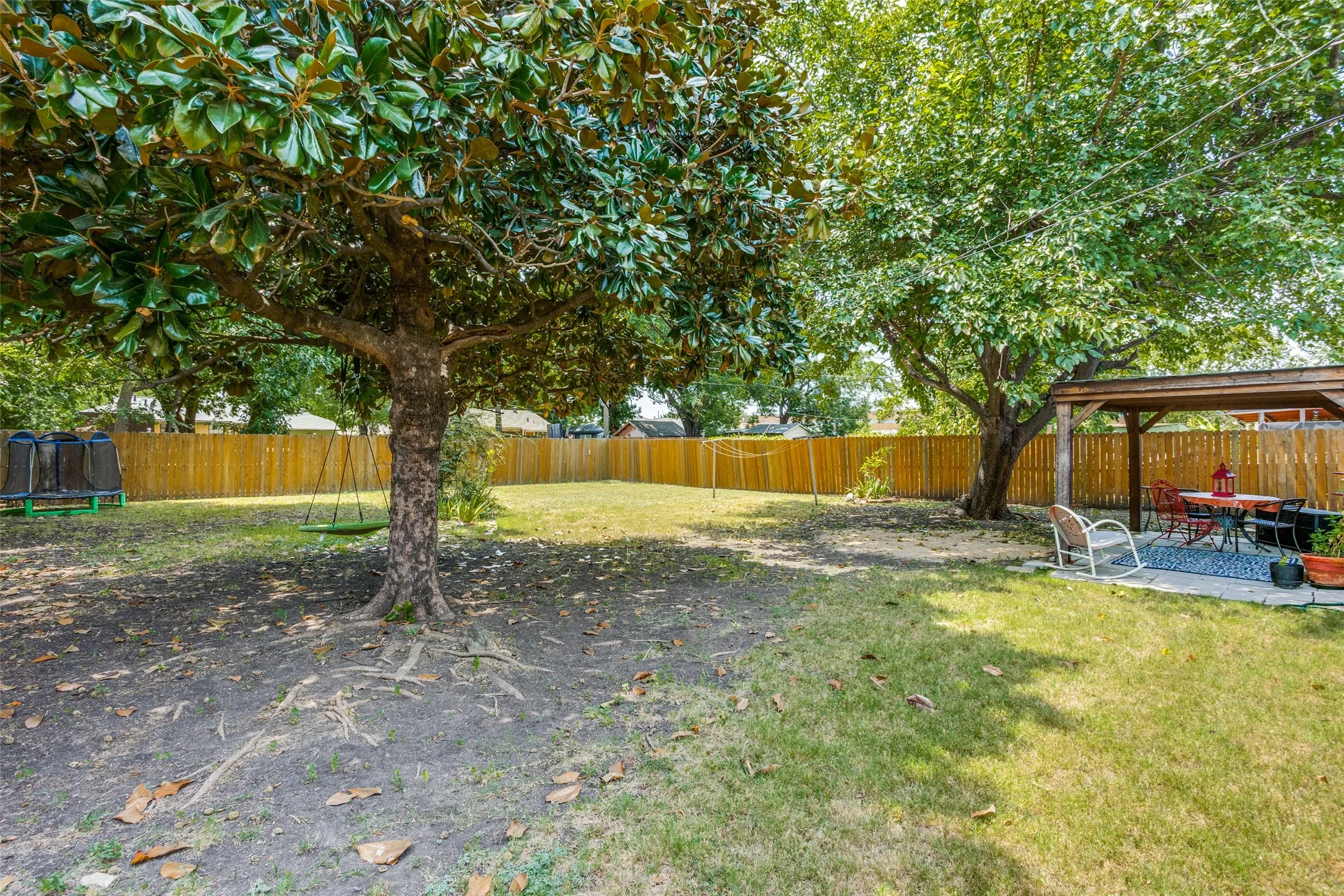 Expansive backyard featuring a wood privacy fence, mature trees, and a covered patio with a wooden pergola