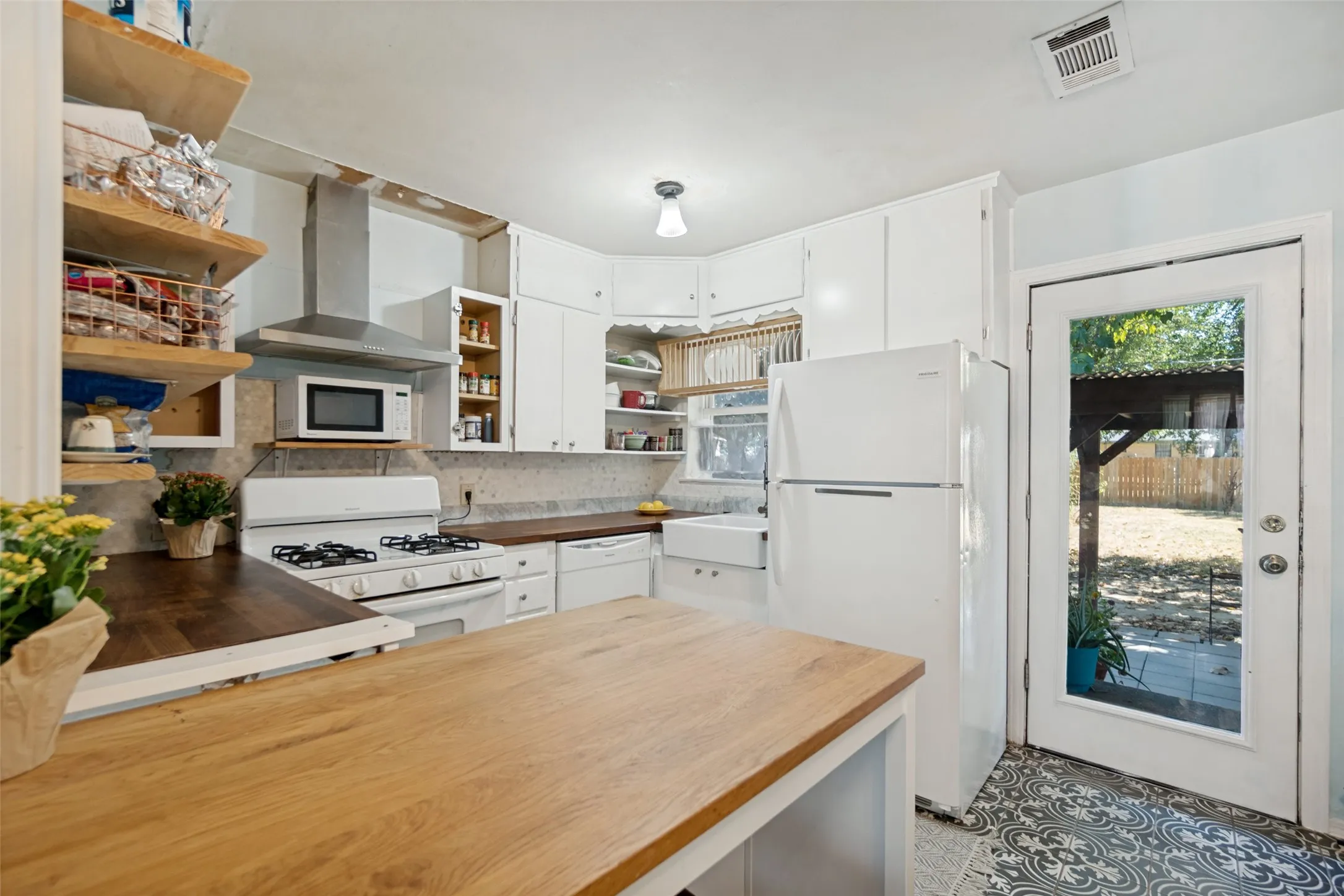 Kitchen with white cabinetry, wood-finish countertops, stainless steel range hood, and patterned floor tiling