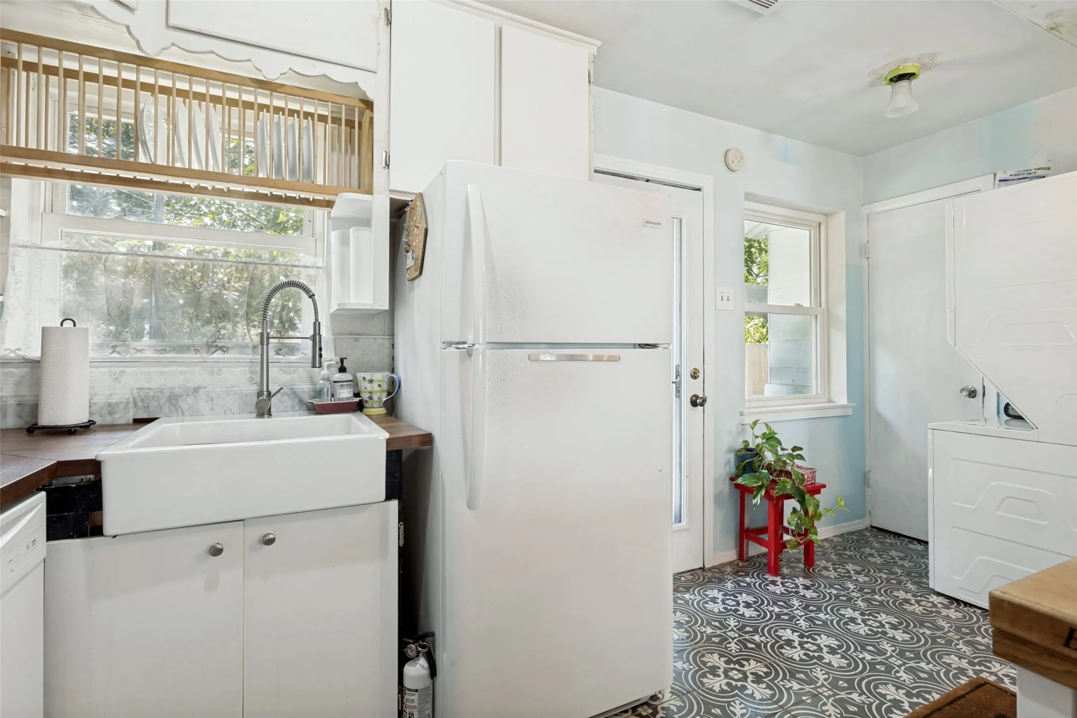 Kitchen featuring white cabinetry, a farmhouse sink, wood-finish countertops, a window over the sink, and patterned floor tile