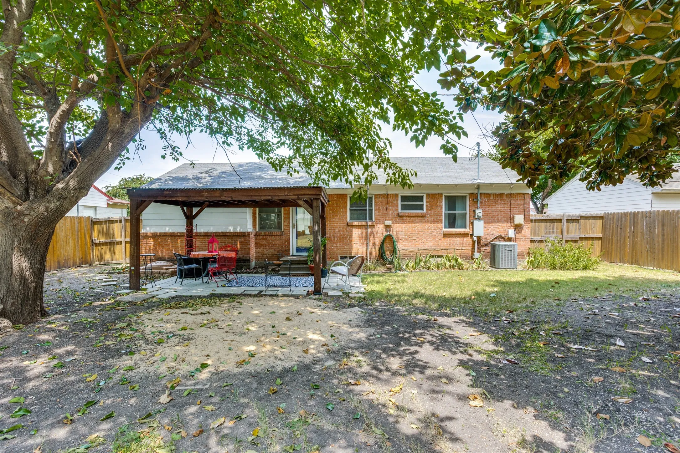 Expansive backyard featuring a wood pergola over a paved patio, mature trees, and a privacy fence