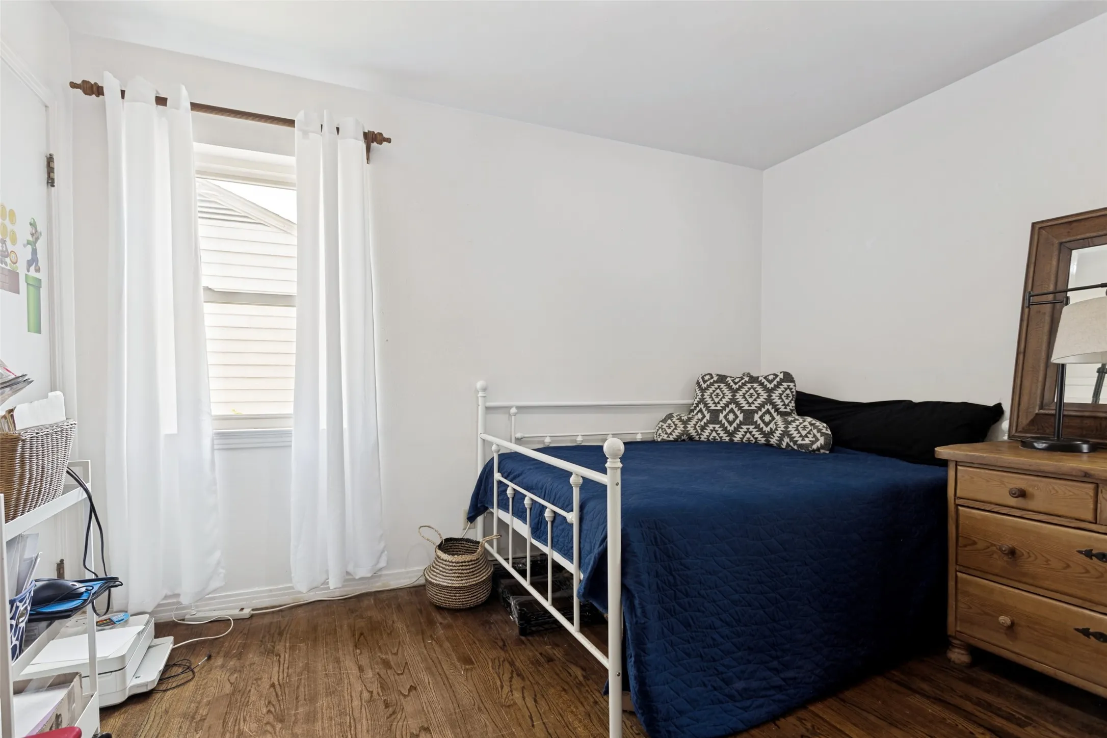 Wood-finish flooring, white painted walls, and a single window with white curtains