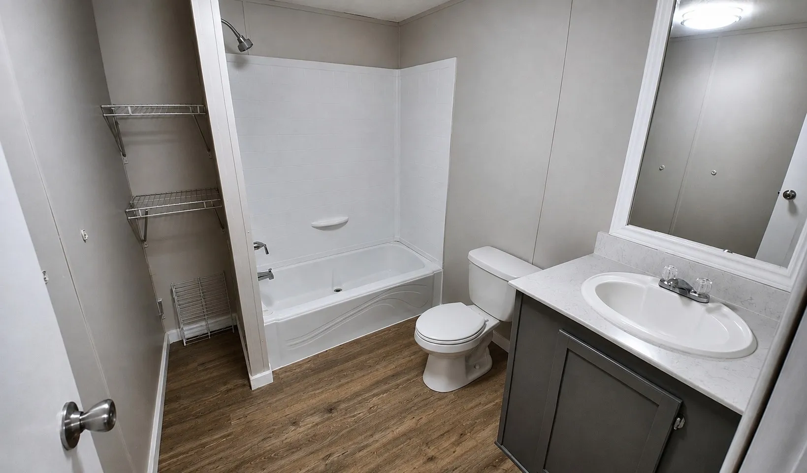 Modern full bathroom featuring a ceramic pedestal sink with chrome fixtures, white subway tile shower/tub combo with glass enclosure, porcelain toilet, wood-finish flooring, and ample storage cabinetry beneath the vanity