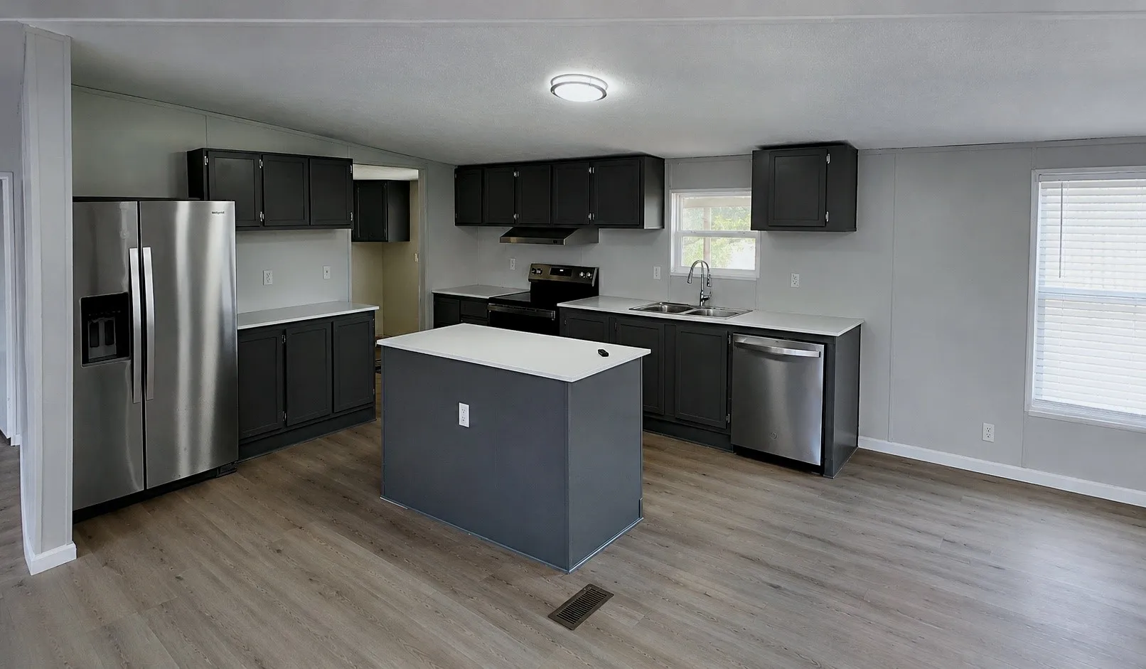 Spacious kitchen with wood-finish flooring, dark cabinetry, a central island, and stainless steel appliances