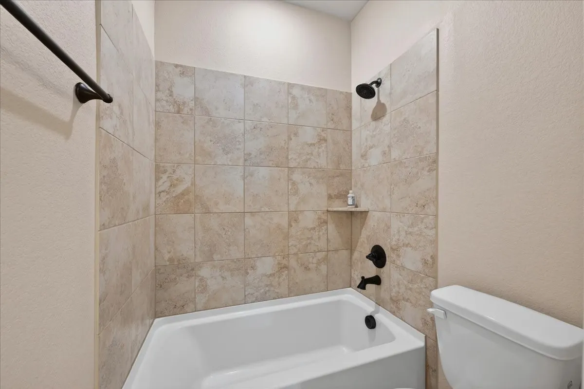 Bathtub with tile surround featuring a built-in shower niche and dark bronze fixtures