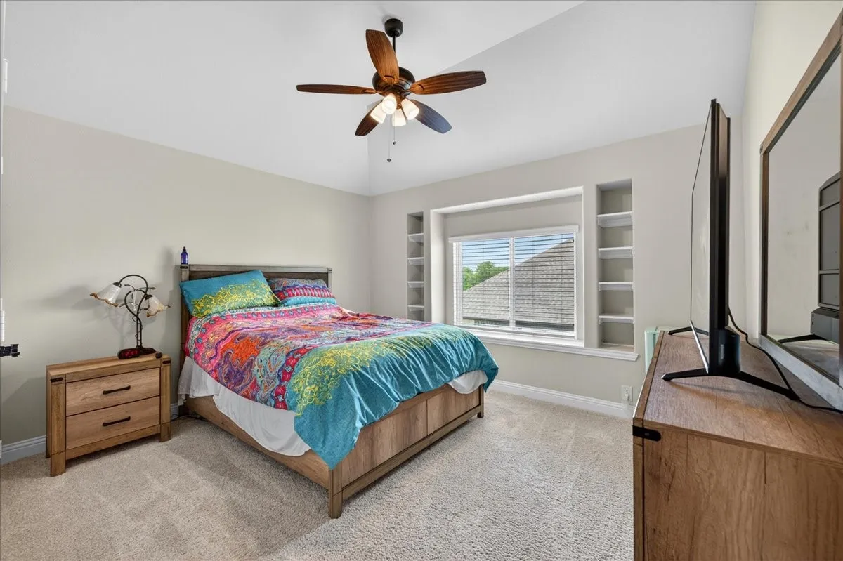 3rd bedroom has light carpeted room featuring a window with built-in shelving, a ceiling fan, and light gray wall paint