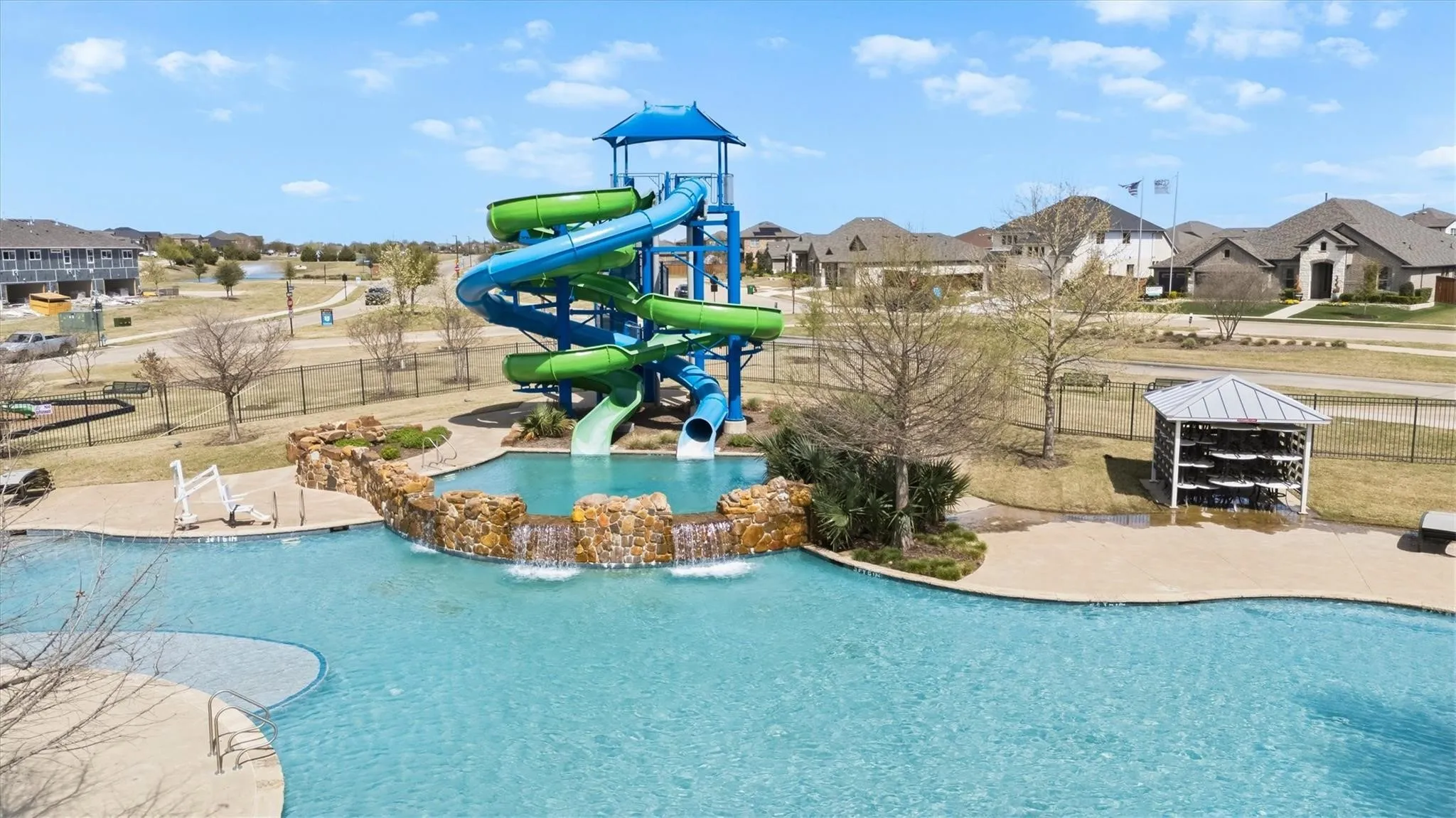 Resort-style aquatic amenity featuring a multi-level water slide structure, a free-form swimming pool with a rock waterfall, and an adjacent splash pad