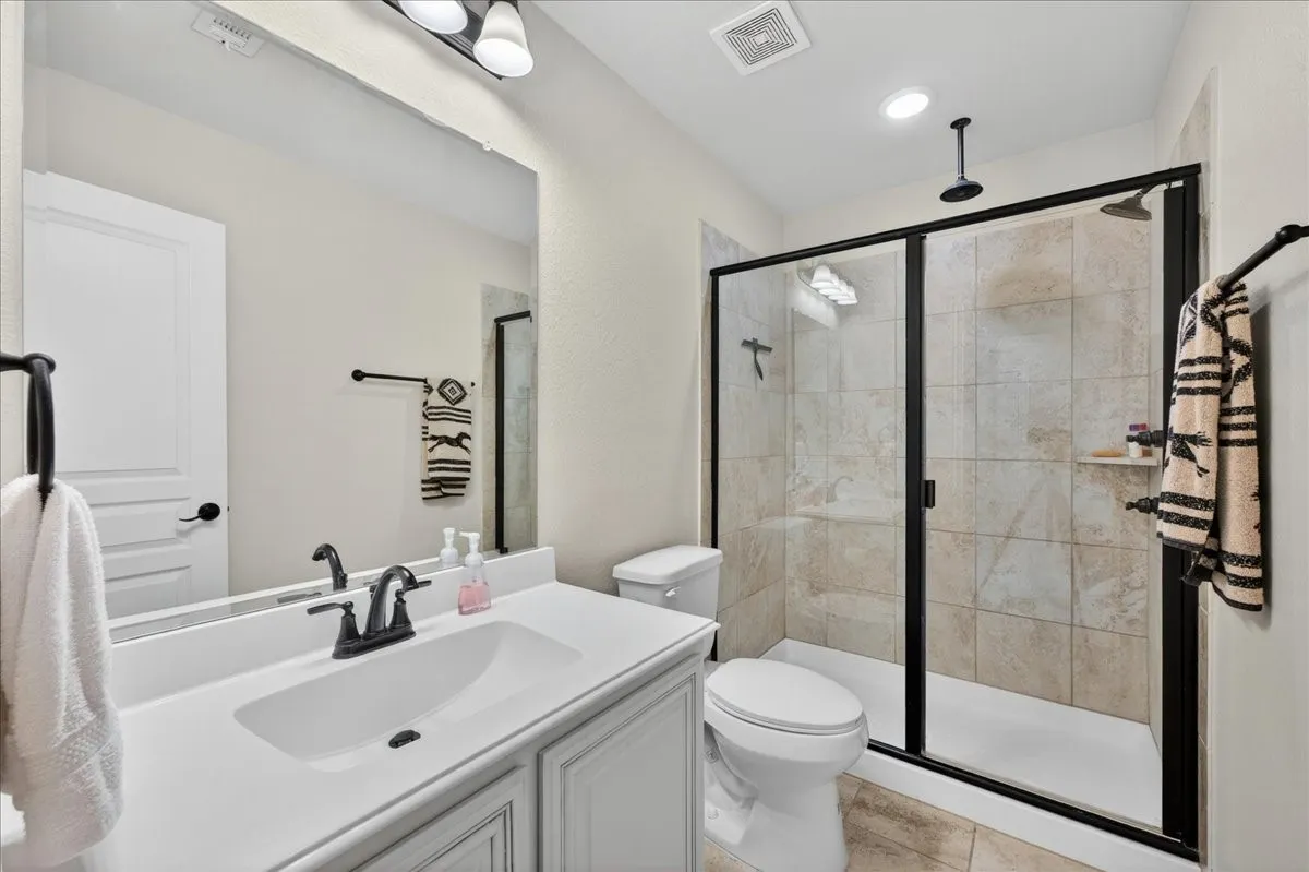 Bathroom featuring a vanity with an integrated sink, a large mirror, and a walk-in shower with a glass enclosure